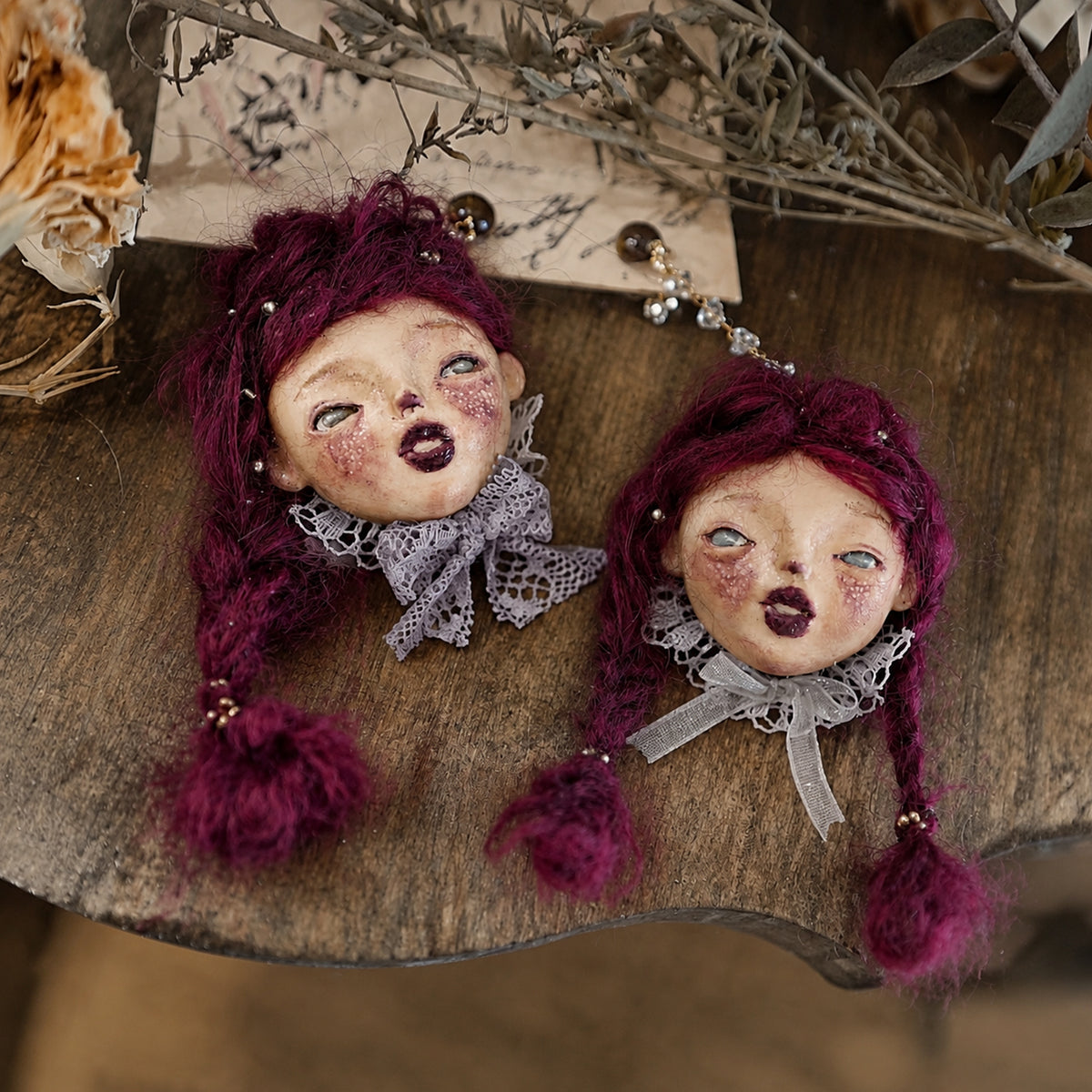 Pair of purple-haired Lambwick doll earrings arranged together on a wooden tray.