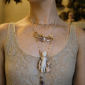 Charlotte ceramic-doll necklace worn over a pale lace top, showing its long layered design.