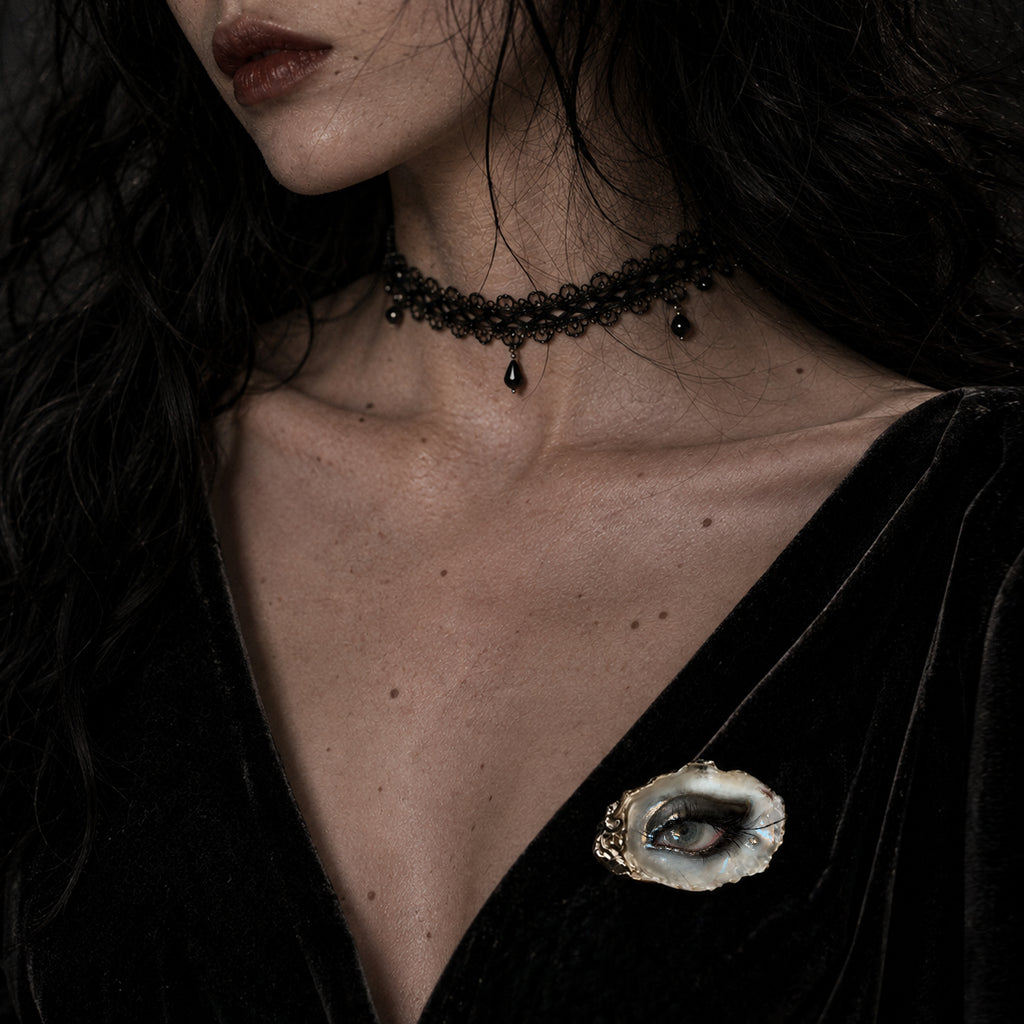 Lilith Veil Black Smoky shell-eye brooch worn on a black V-neck top.
