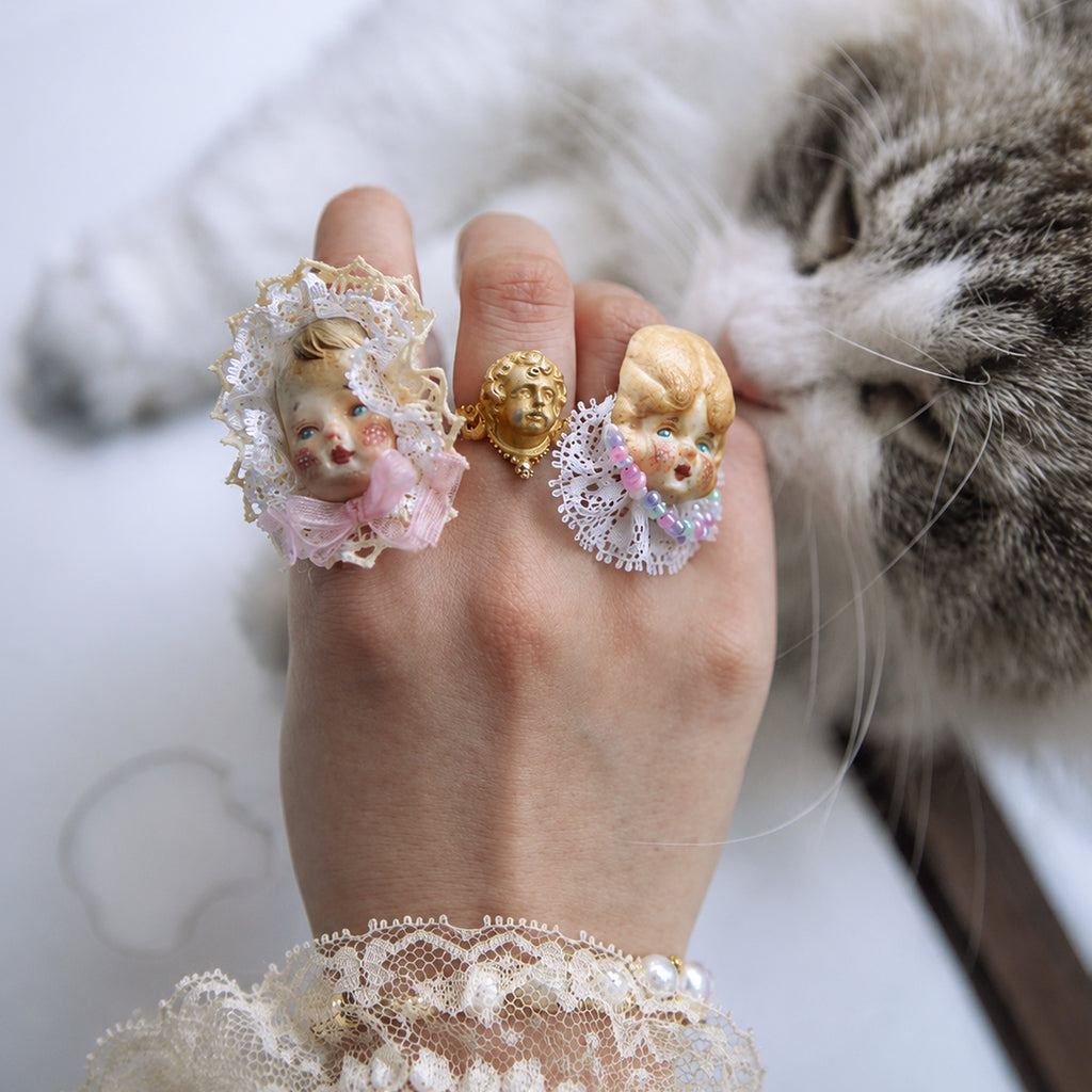 Two Lambwick doll-face rings worn on adjacent fingers beside a cat.