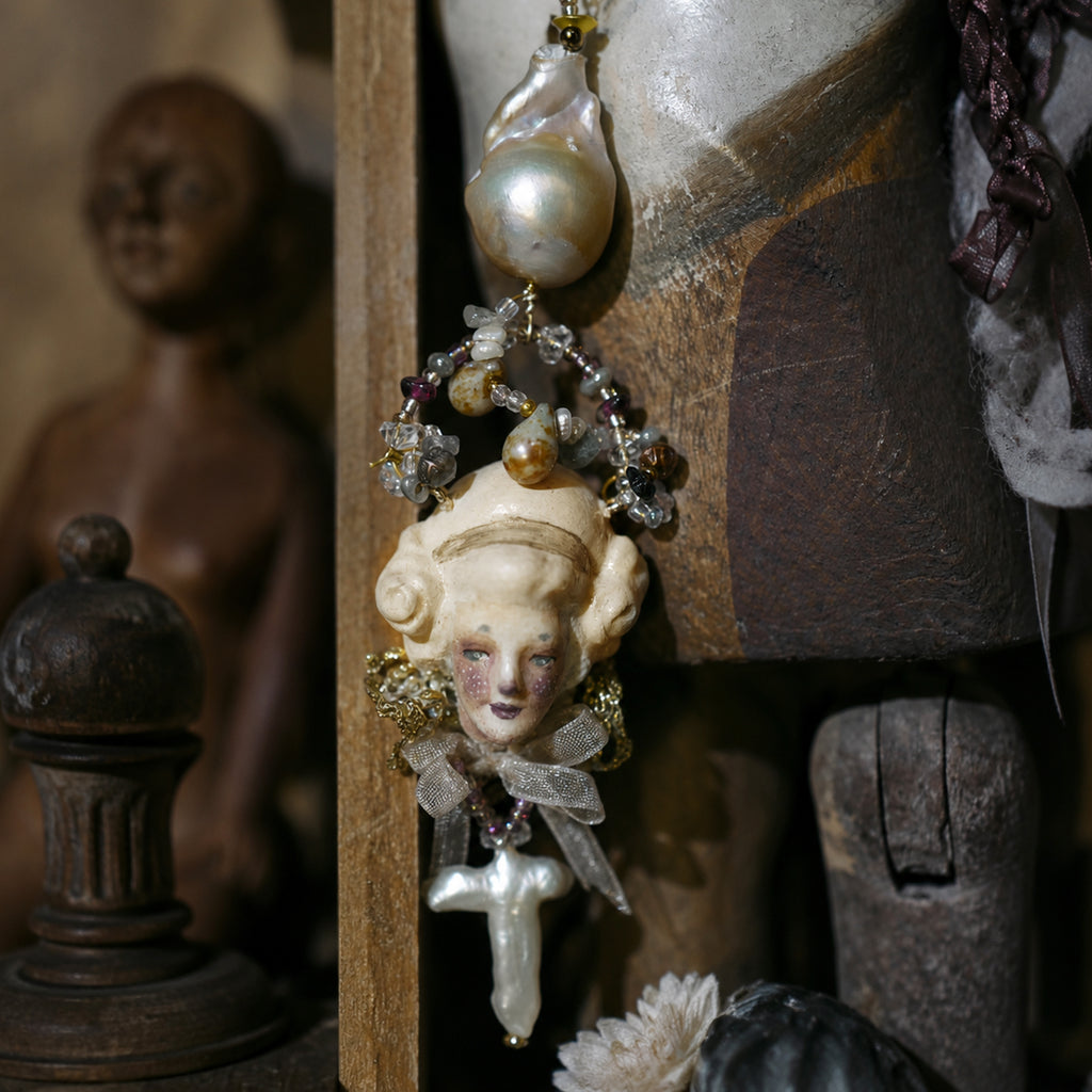 Close-up of an Odette Cross doll face, large pale bead and hanging cross.