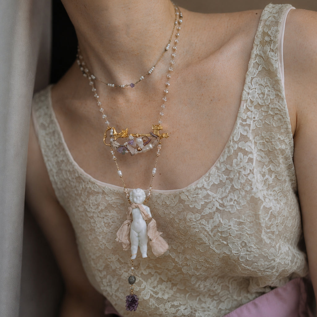 Charlotte ceramic-doll necklace shown on an ivory lace top.