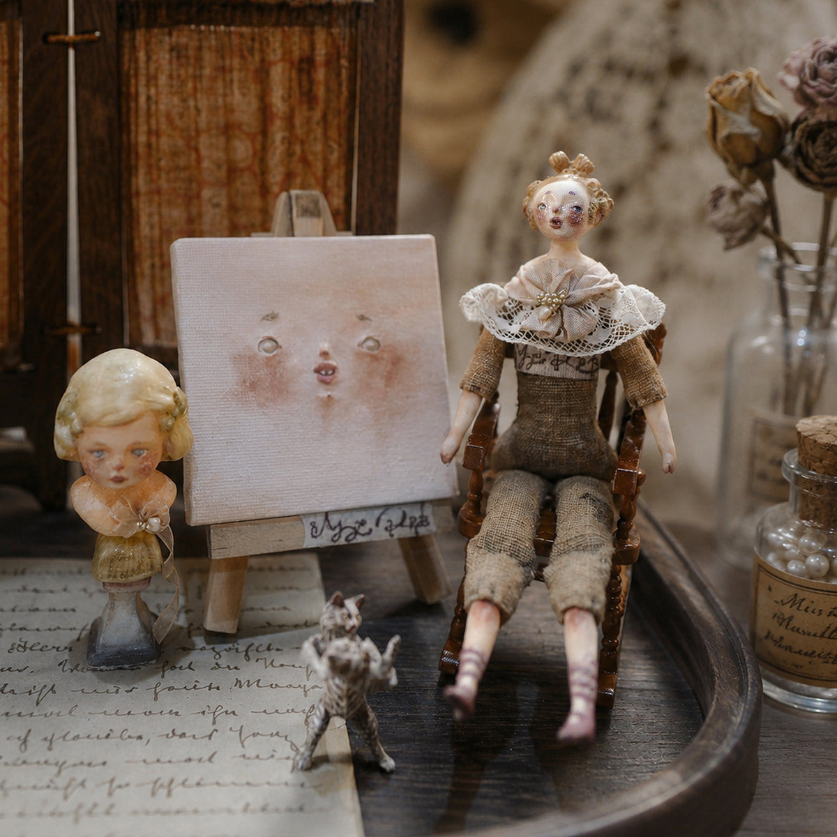 Lambwick seated art doll on its wooden chair beside a miniature portrait bust and an artwork card.