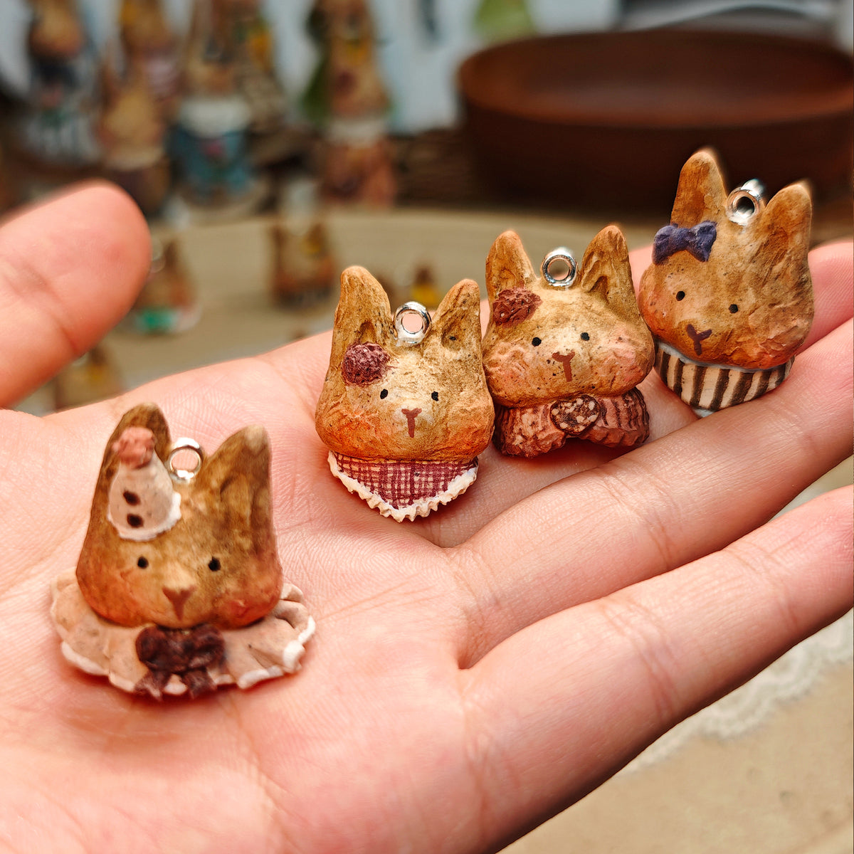 Four Winterwood rabbit pendants with different bows and collars, held in a hand.