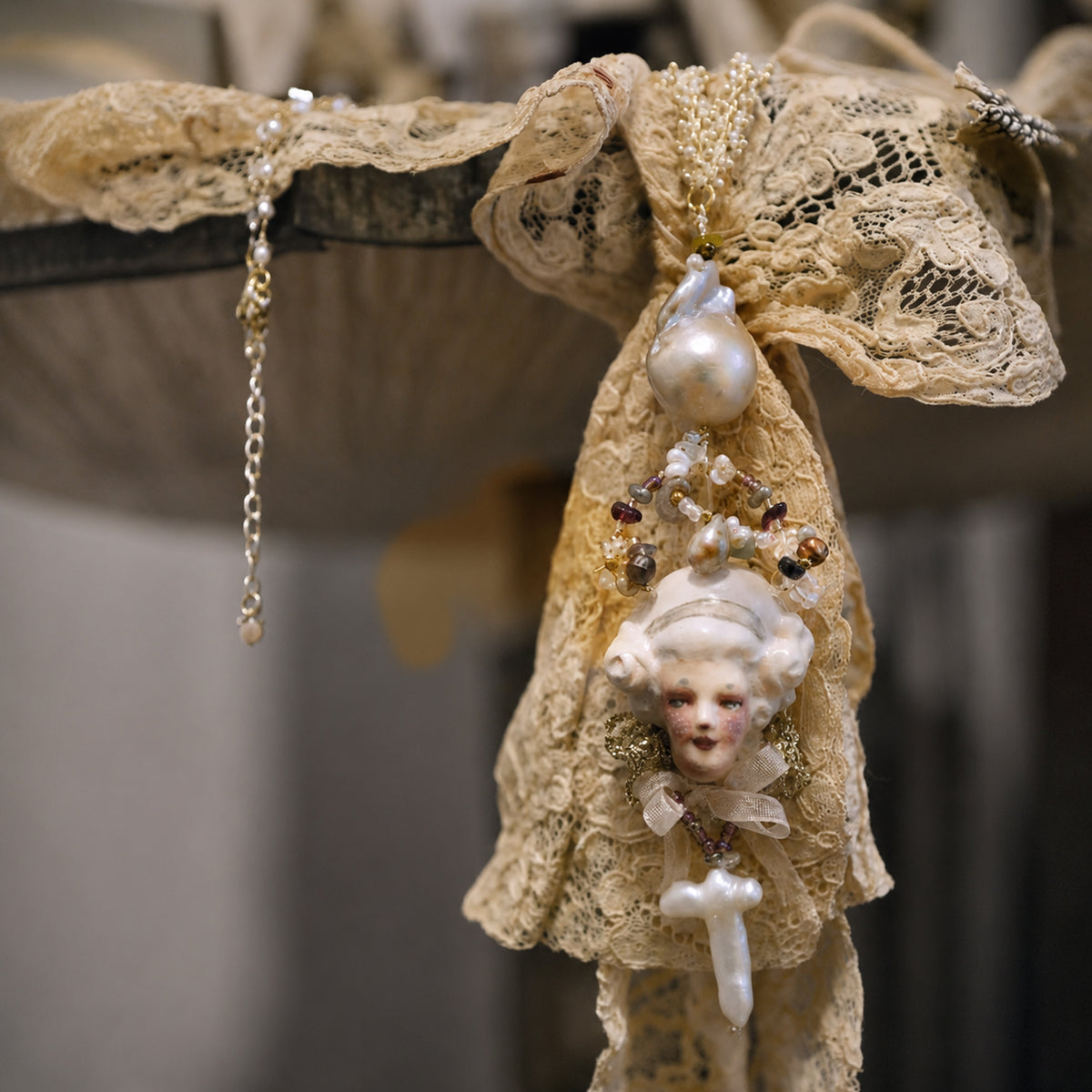 Odette Cross doll necklace draped over cream lace, showing the sculpted face and cross.