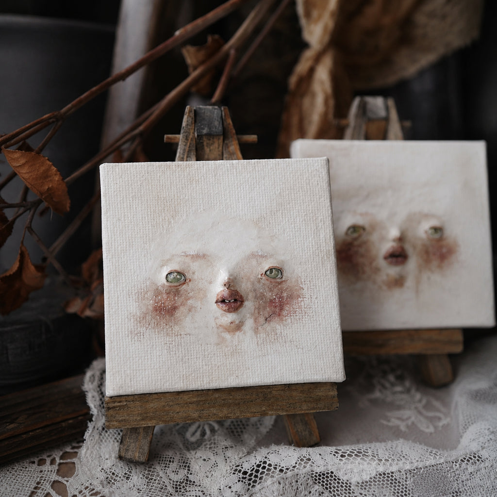 Close view of two Lambwick clay-relief face artworks on miniature easels.