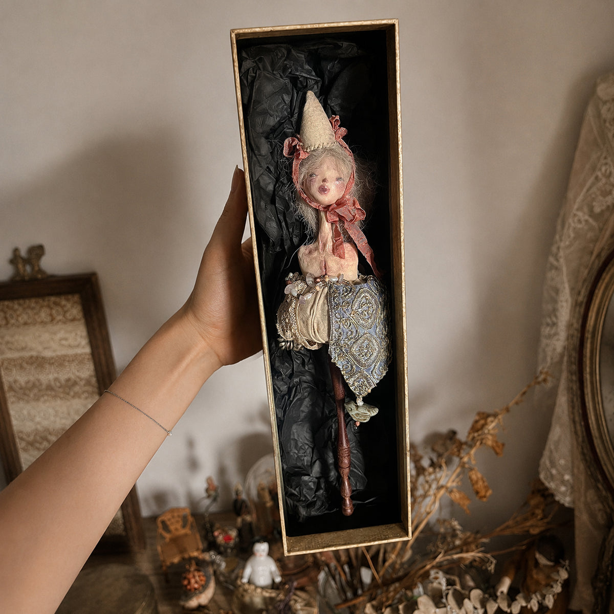Lambwick doll hand-bell sculpture in its long open presentation box, held upright.