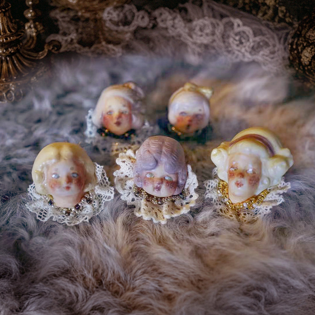 Five Lambwick doll ring designs arranged together on soft feathers.