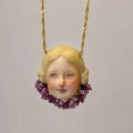 Blonde Lambwick doll-face pendant with a purple lace collar on a gold-tone chain.