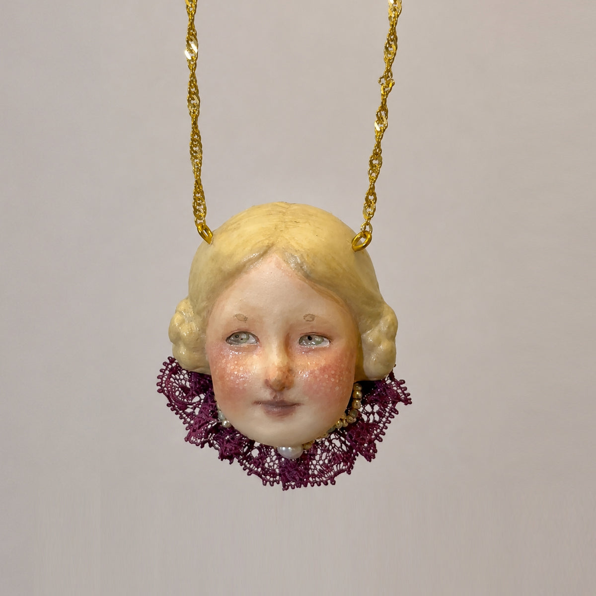 Blonde Lambwick doll-face pendant with a purple lace collar on a gold-tone chain.