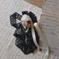 Masked Lambwick doll brooch with black lace, a pale ribbon and a mint-colored bow.