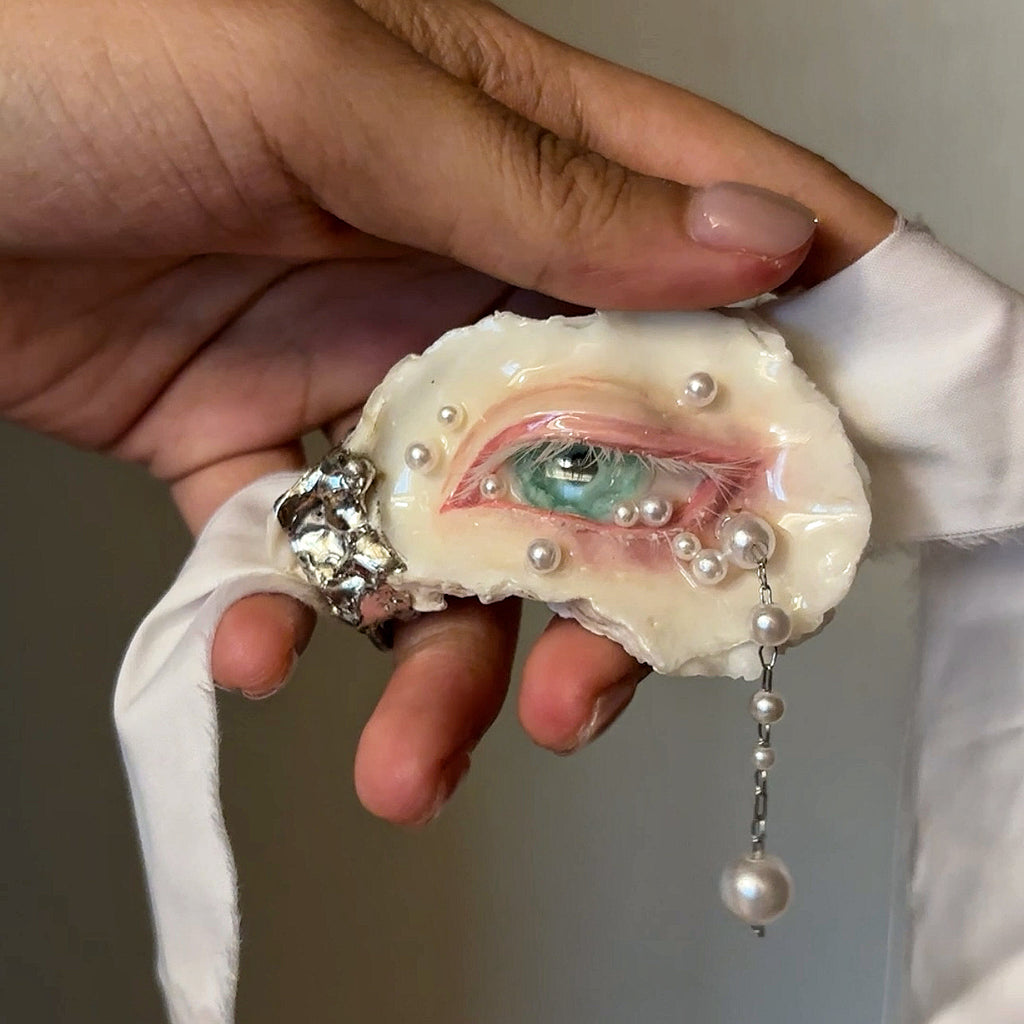 Nyra Seafoam Gaze oyster eye attached to pale ribbon, held in a hand.