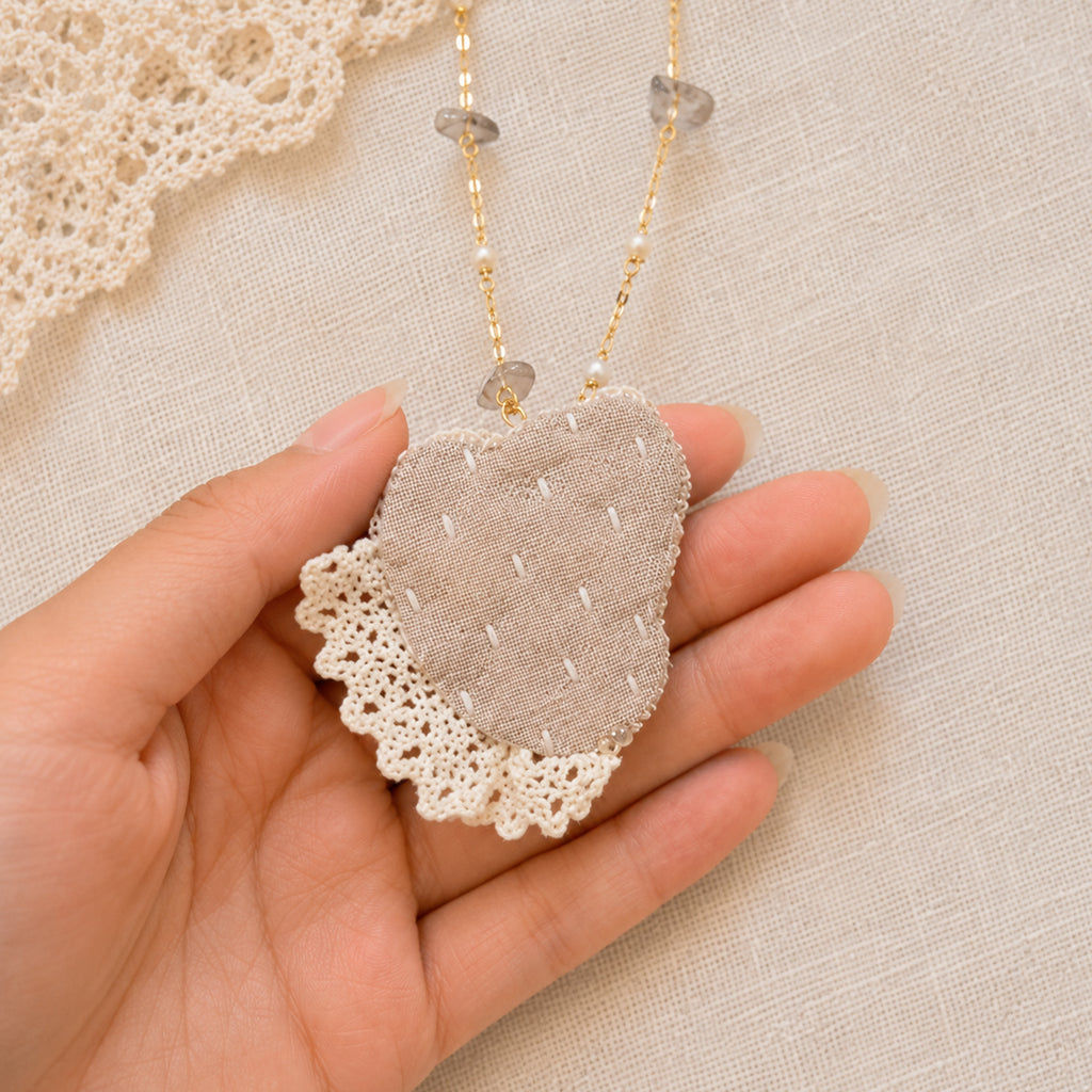 Back of a Lambwick doll-face pendant with stitched fabric and pale lace, held in a hand.