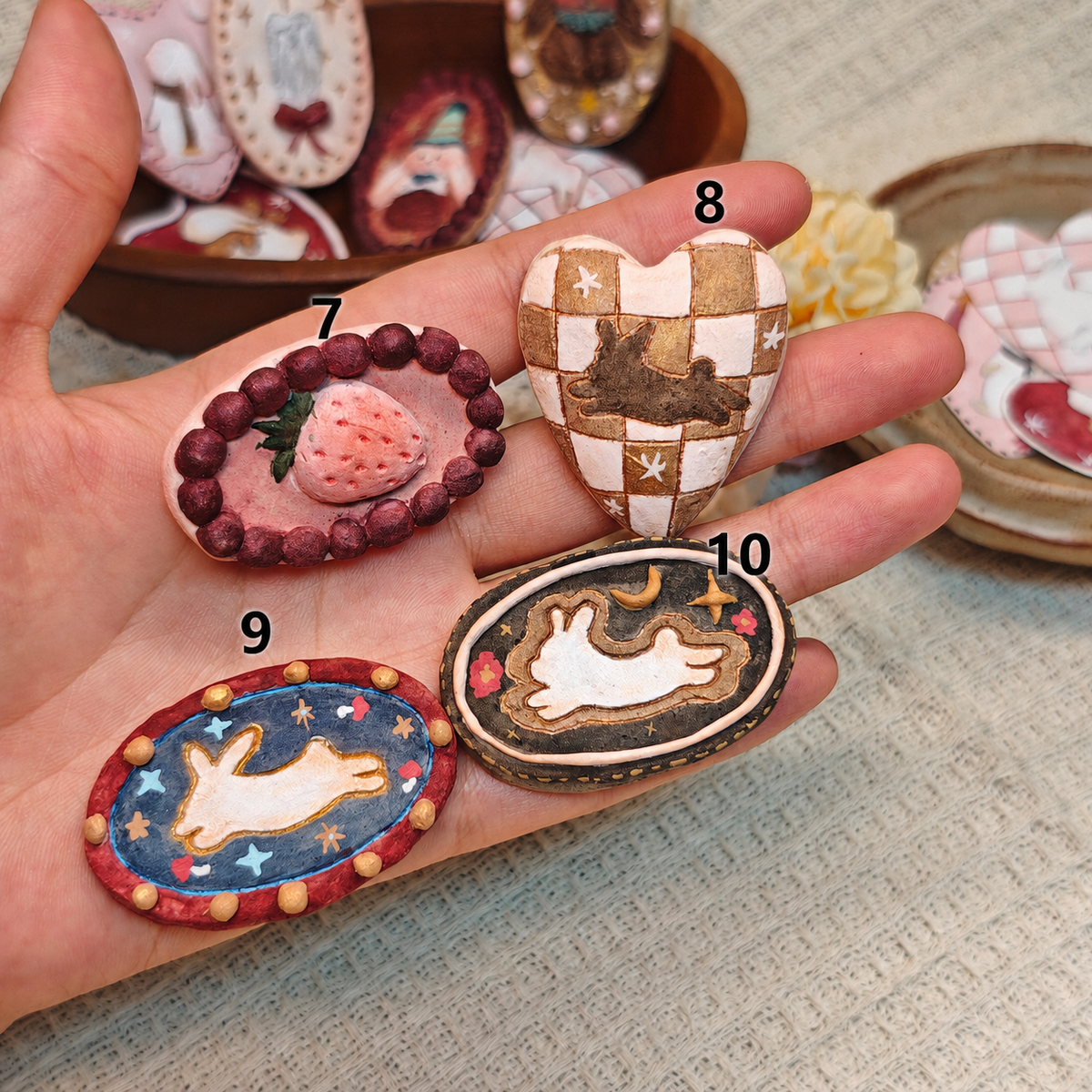 Winterwood strawberry, checked-heart and rabbit-motif brooches held together in a hand.
