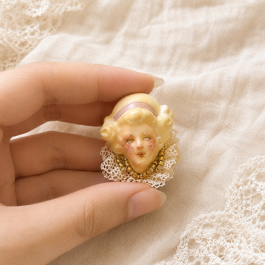 Lambwick doll ring with golden curls and a pink headband, held against cream lace.