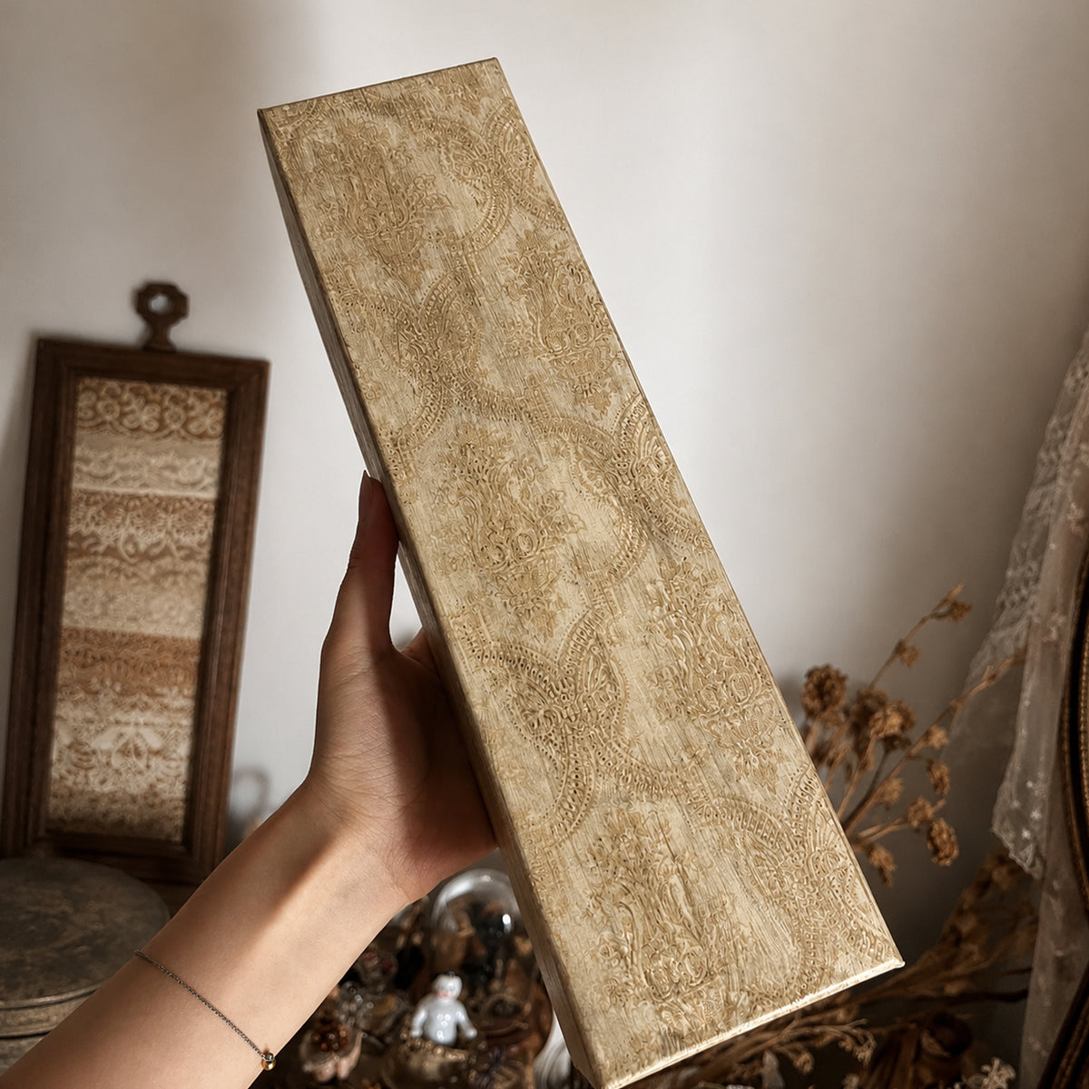 Closed gold-toned presentation box for the Lambwick doll hand-bell sculpture, held in a hand.