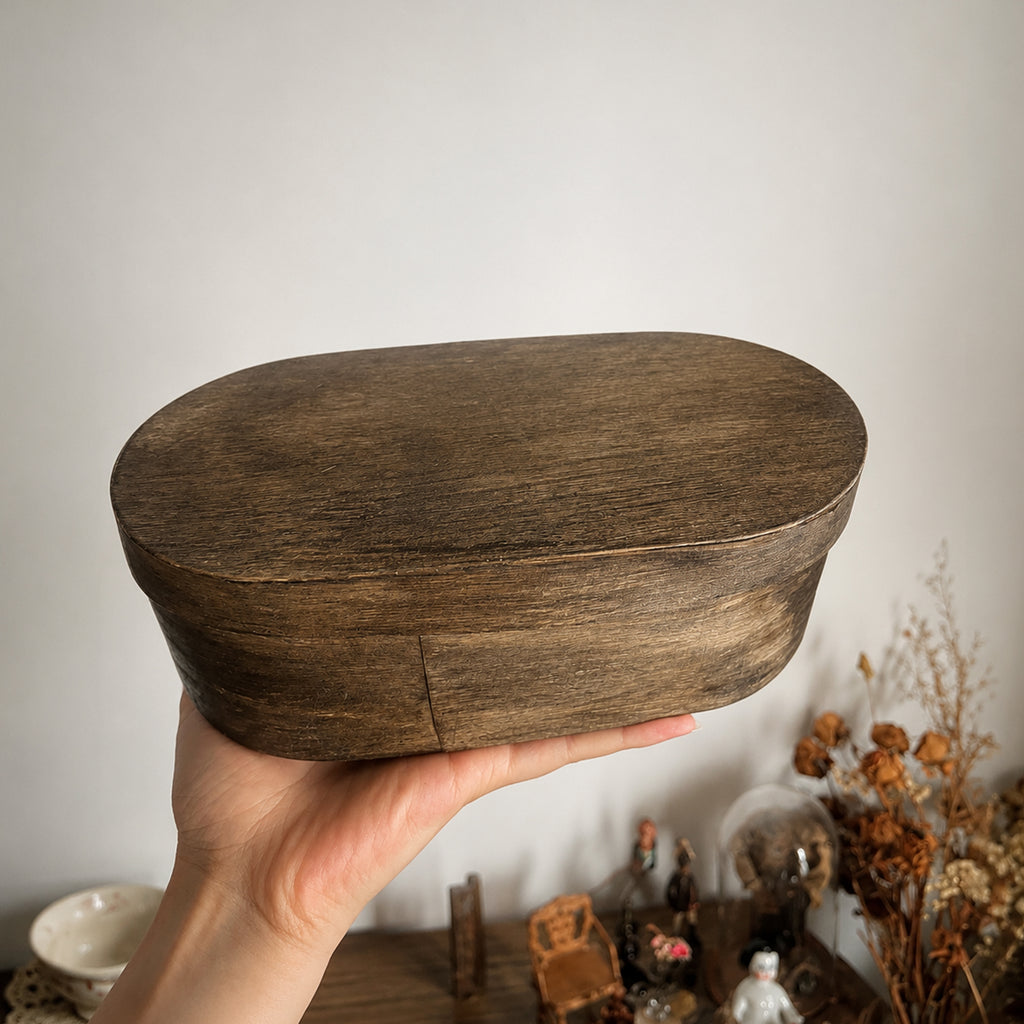 Oval wooden presentation box for the Lambwick art-doll set, held in a hand.