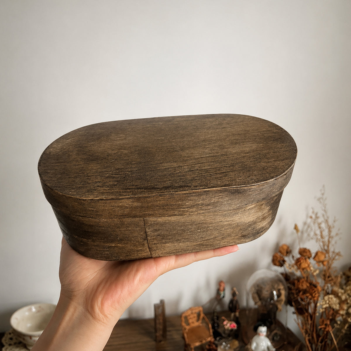 Oval wooden presentation box for the Lambwick art-doll set, held in a hand.