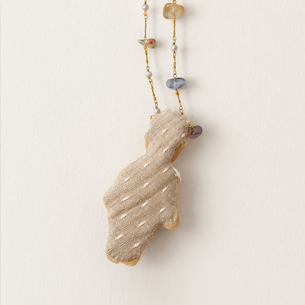 Fabric-covered back of the full-body Lambwick doll pendant and its beaded chain.