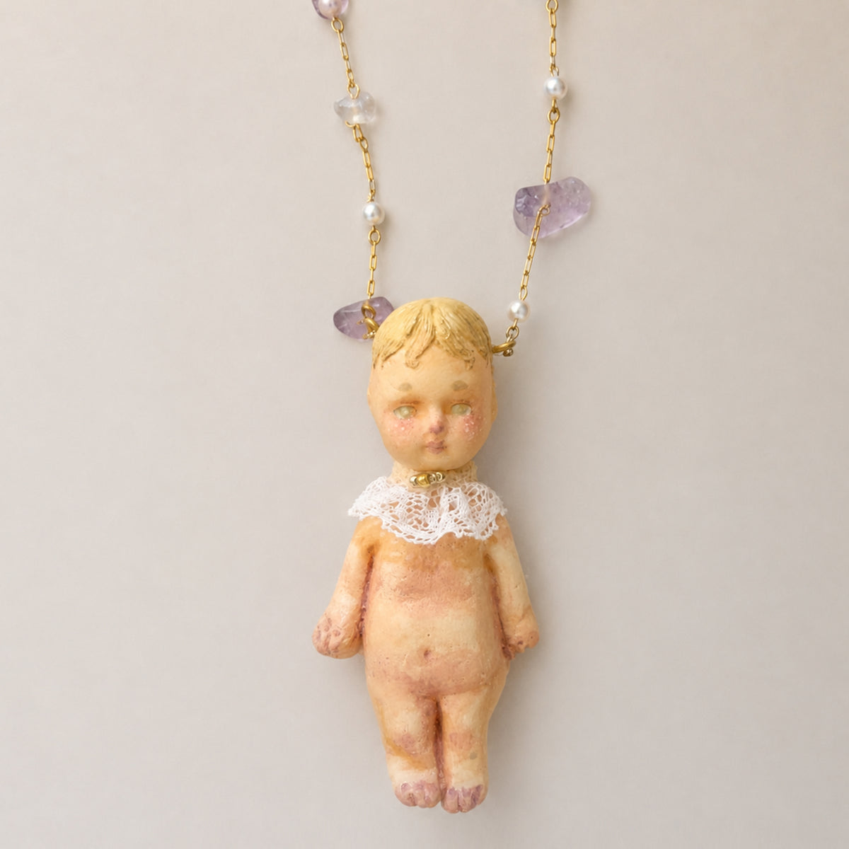 Full-body Lambwick doll pendant with a lace collar and small pastel beads along the chain.