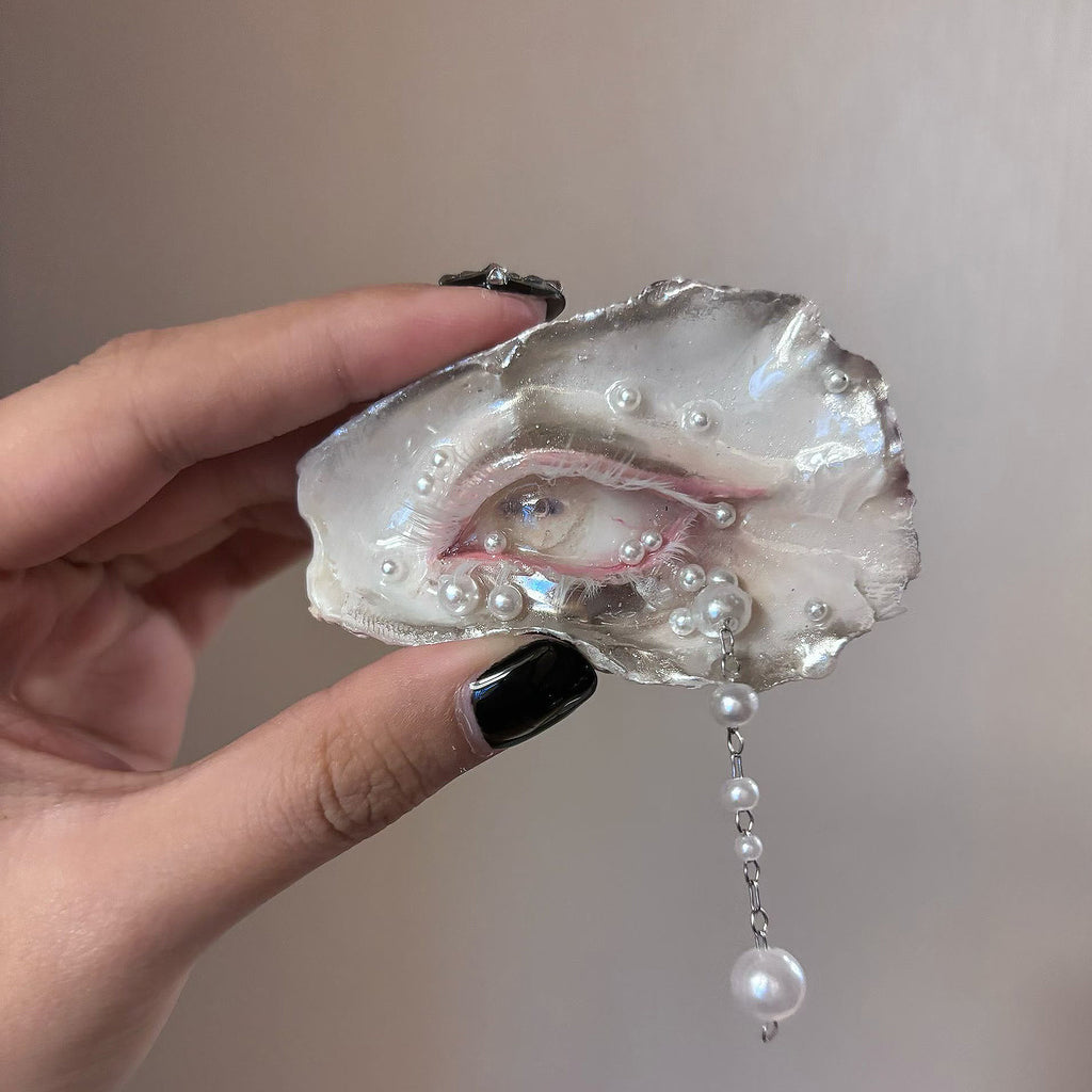 Nyra Lamb Gaze oyster eye held in a hand, showing its horizontal pupil and hanging pearl-like drops.