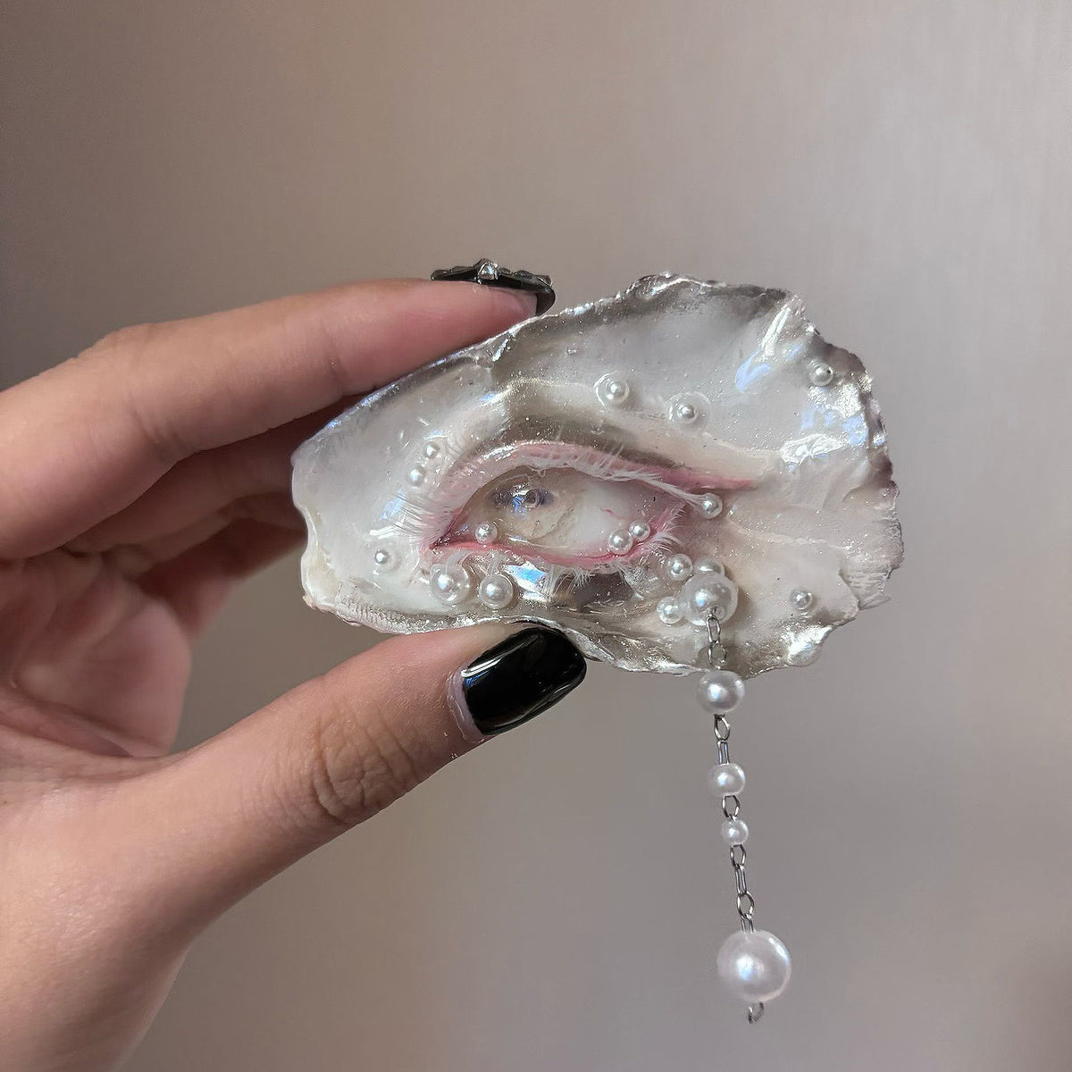 Nyra Lamb Gaze oyster eye held in a hand, showing its horizontal pupil and hanging pearl-like drops.