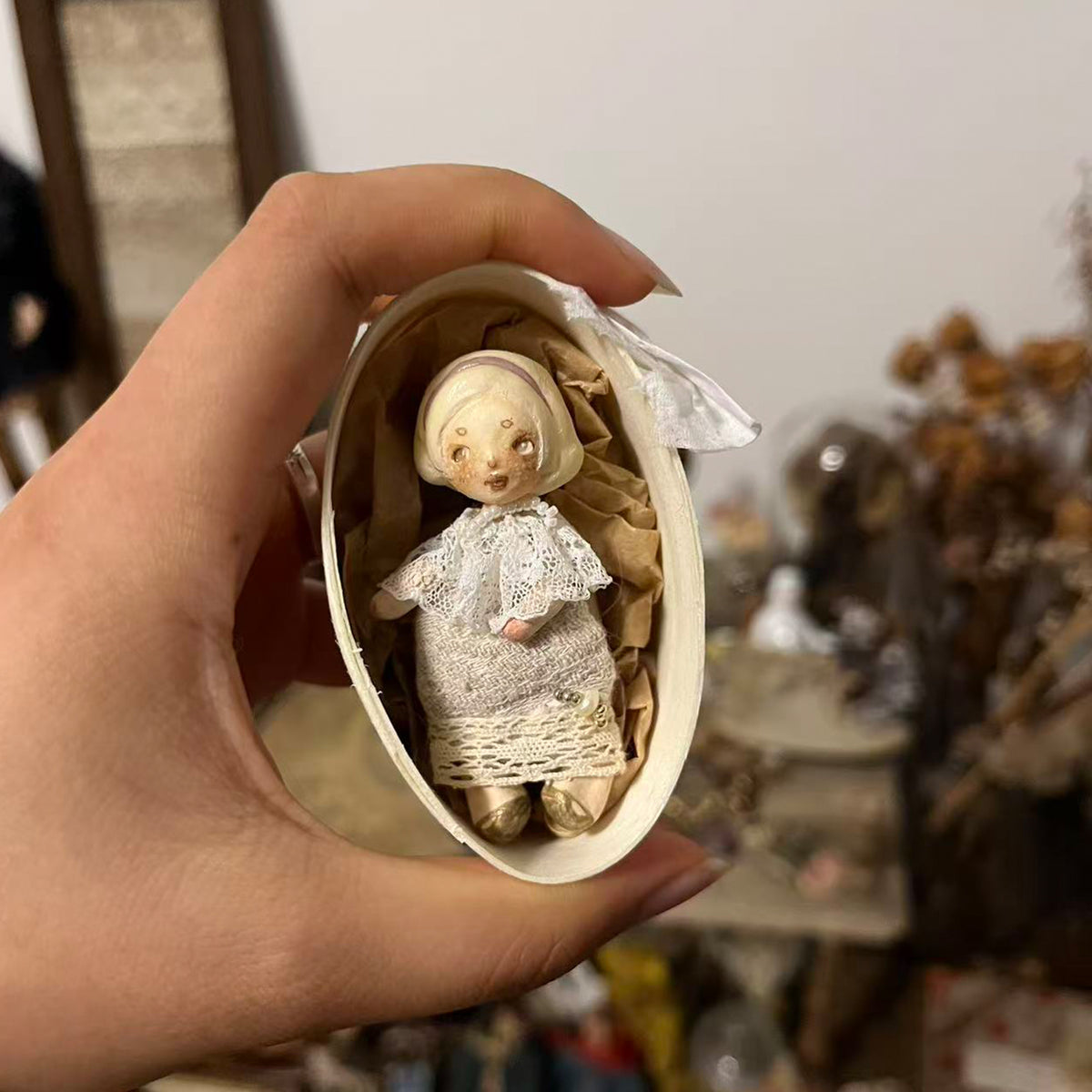 Miniature Lambwick resident doll in an oval presentation box, held in a hand.