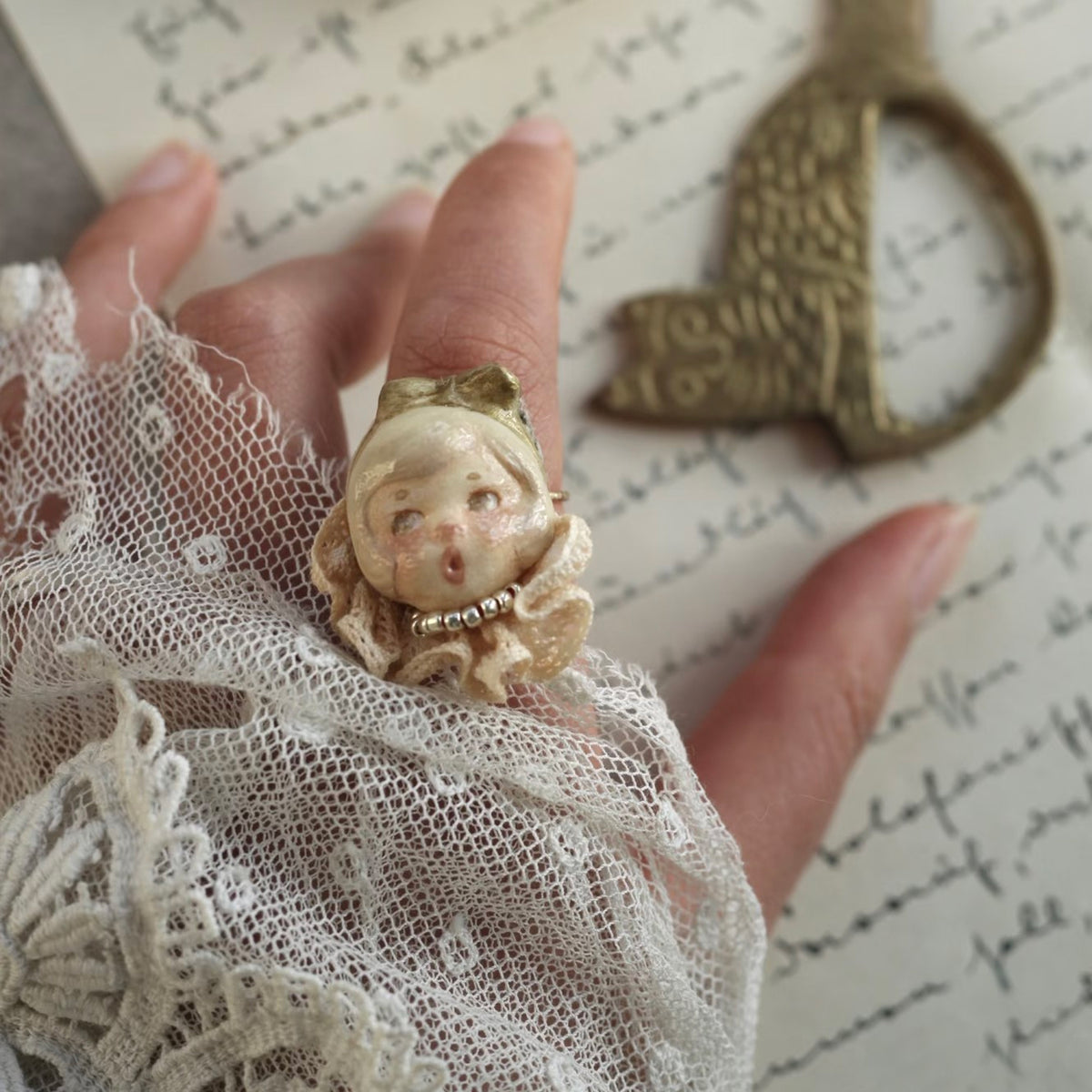 Lambwick mother doll ring with a cream bonnet and lace collar, worn on a finger.