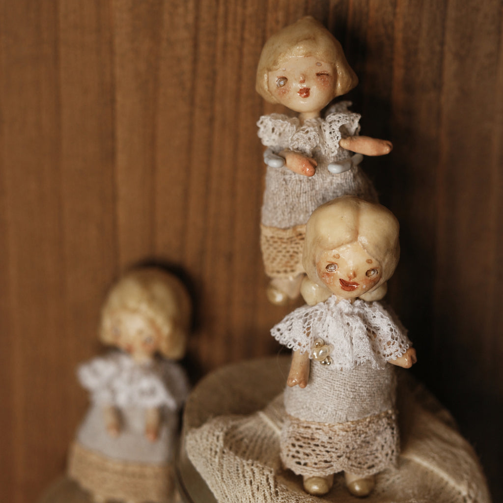 Two miniature Lambwick resident dolls with pale hair, lace collars and grey fabric dresses.