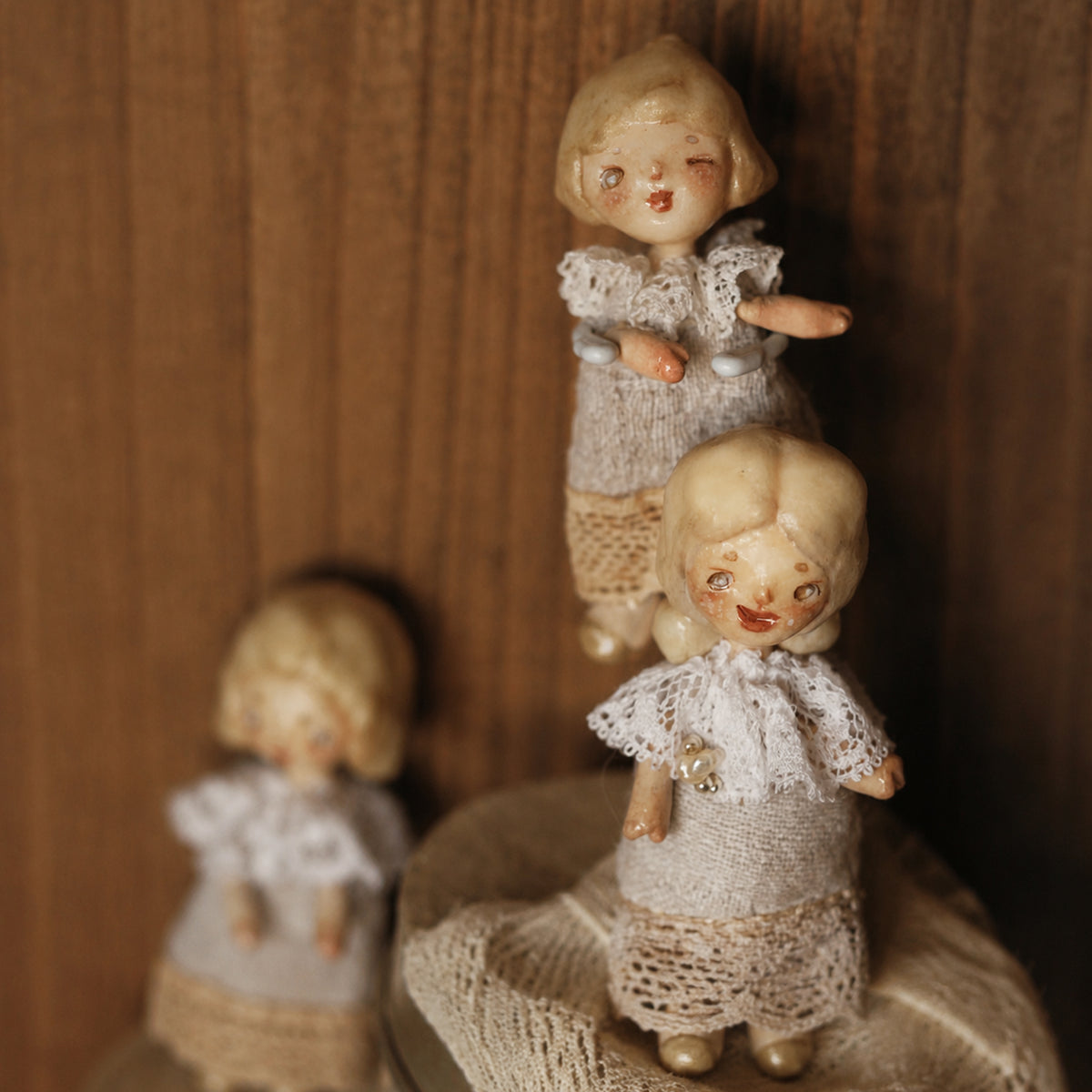 Two miniature Lambwick resident dolls with pale hair, lace collars and grey fabric dresses.