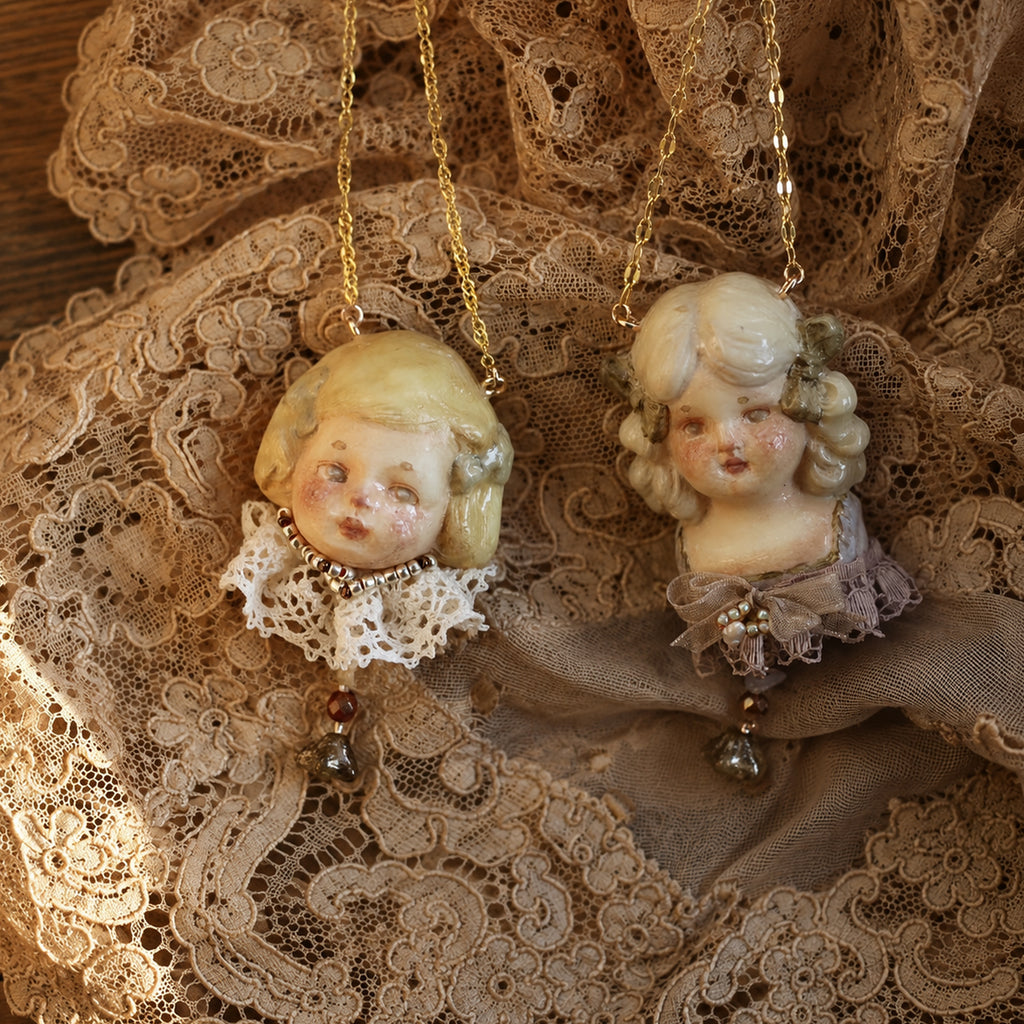 Two blonde Lambwick doll-head necklaces with different lace collars and drop ornaments.