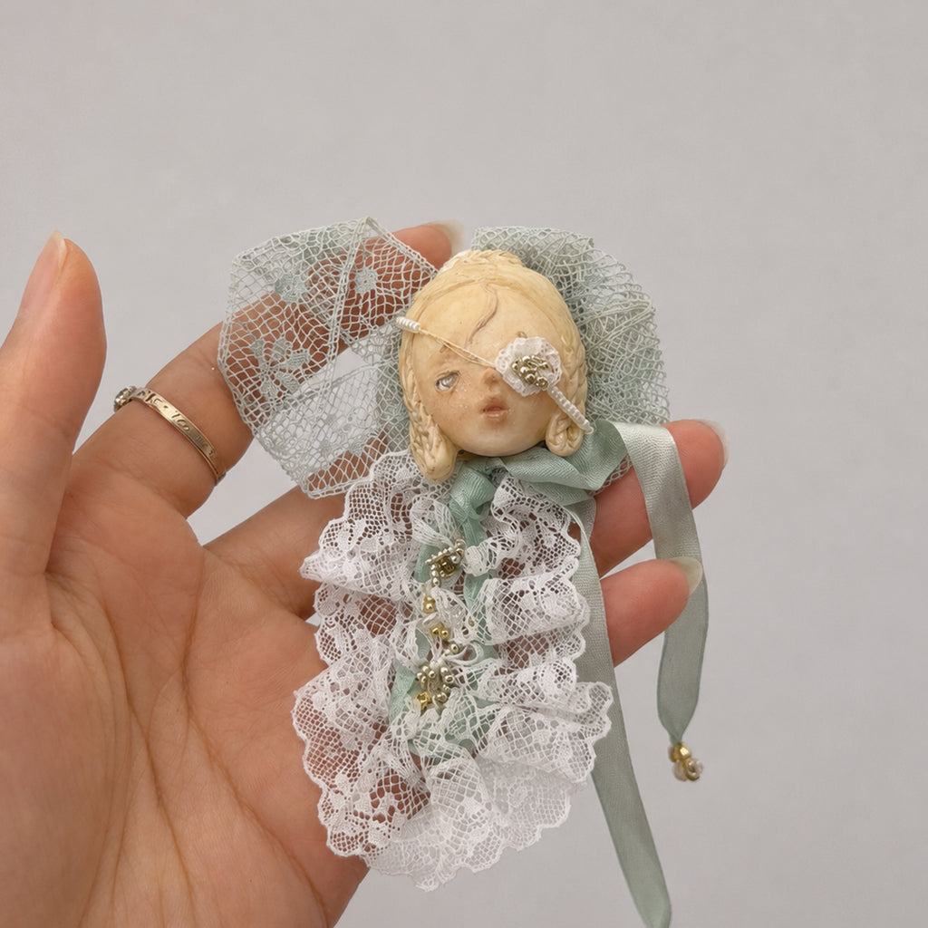 White-lace masked Lambwick doll brooch held in a hand to show its scale.