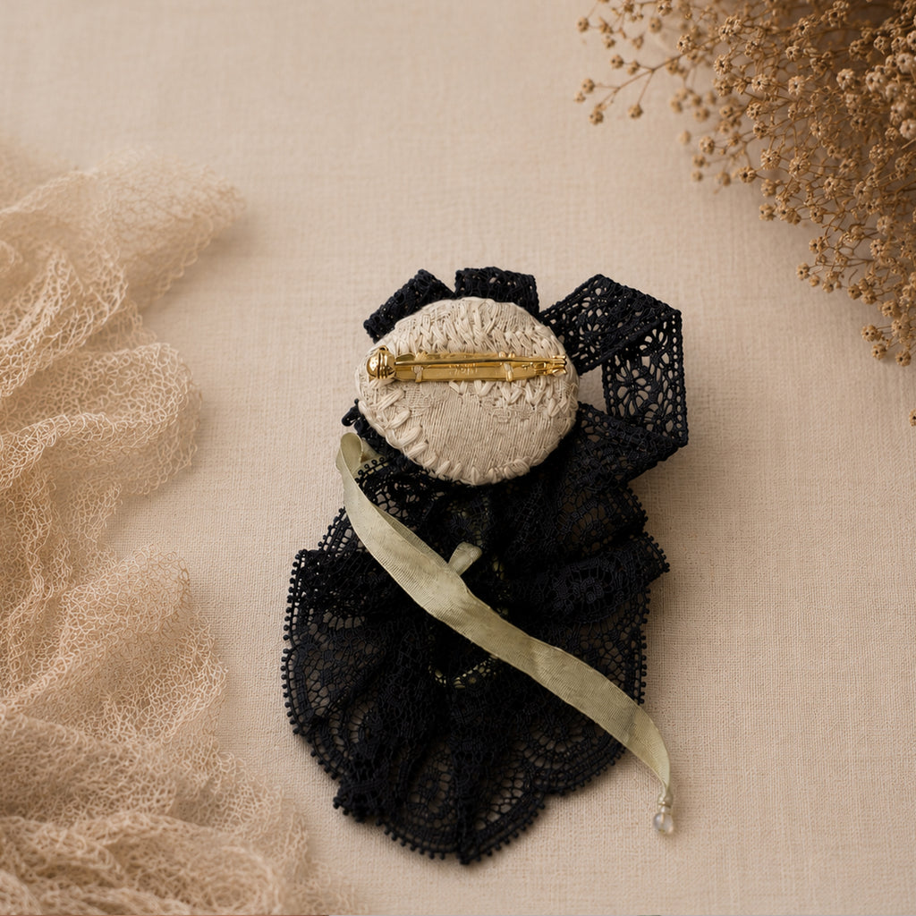 Back of a black-lace Lambwick doll brooch showing the gold-tone pin and fabric backing.