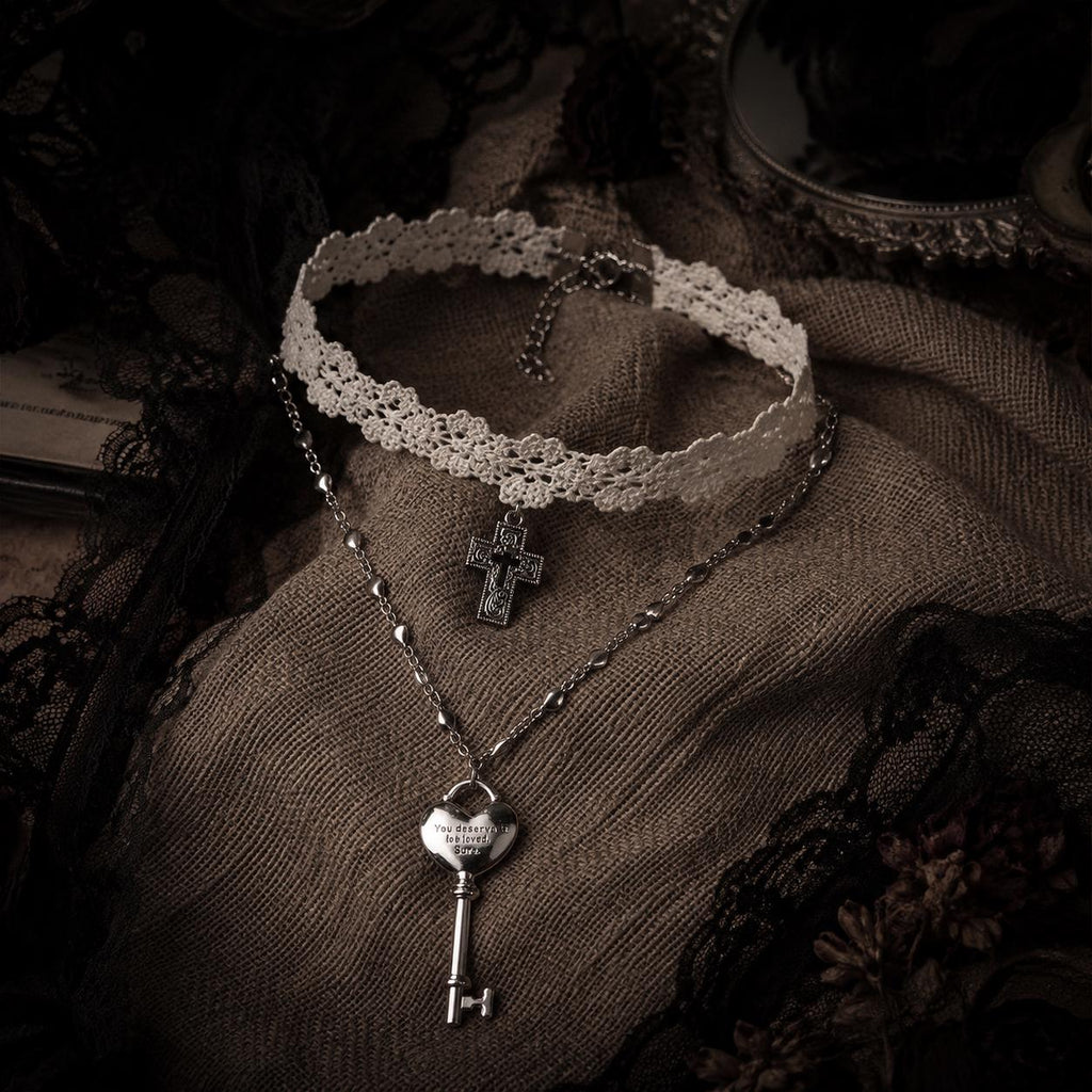 Ivory lace cross choker and heart-key necklace arranged on brown lace.