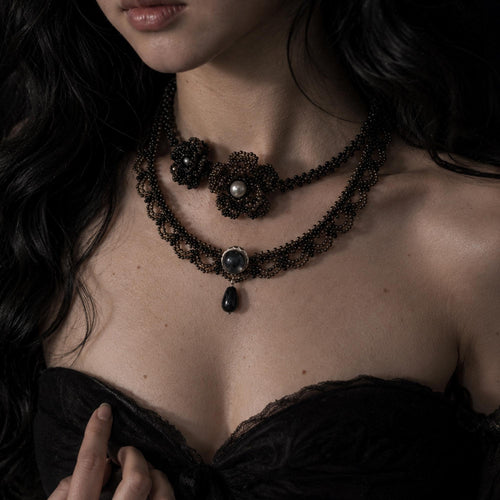 Two black beaded gothic necklaces worn together over a dark neckline.