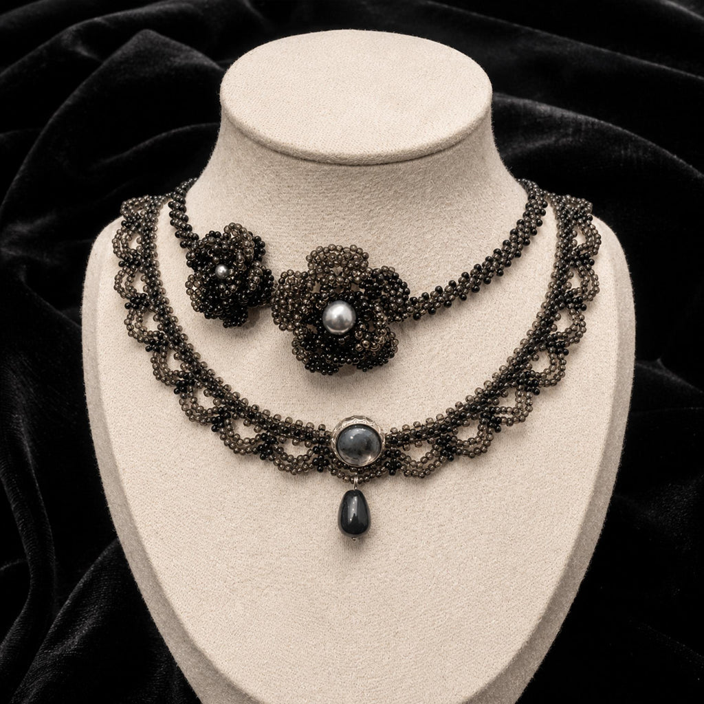 Black floral-center necklace and black teardrop necklace displayed together on a jewelry bust.