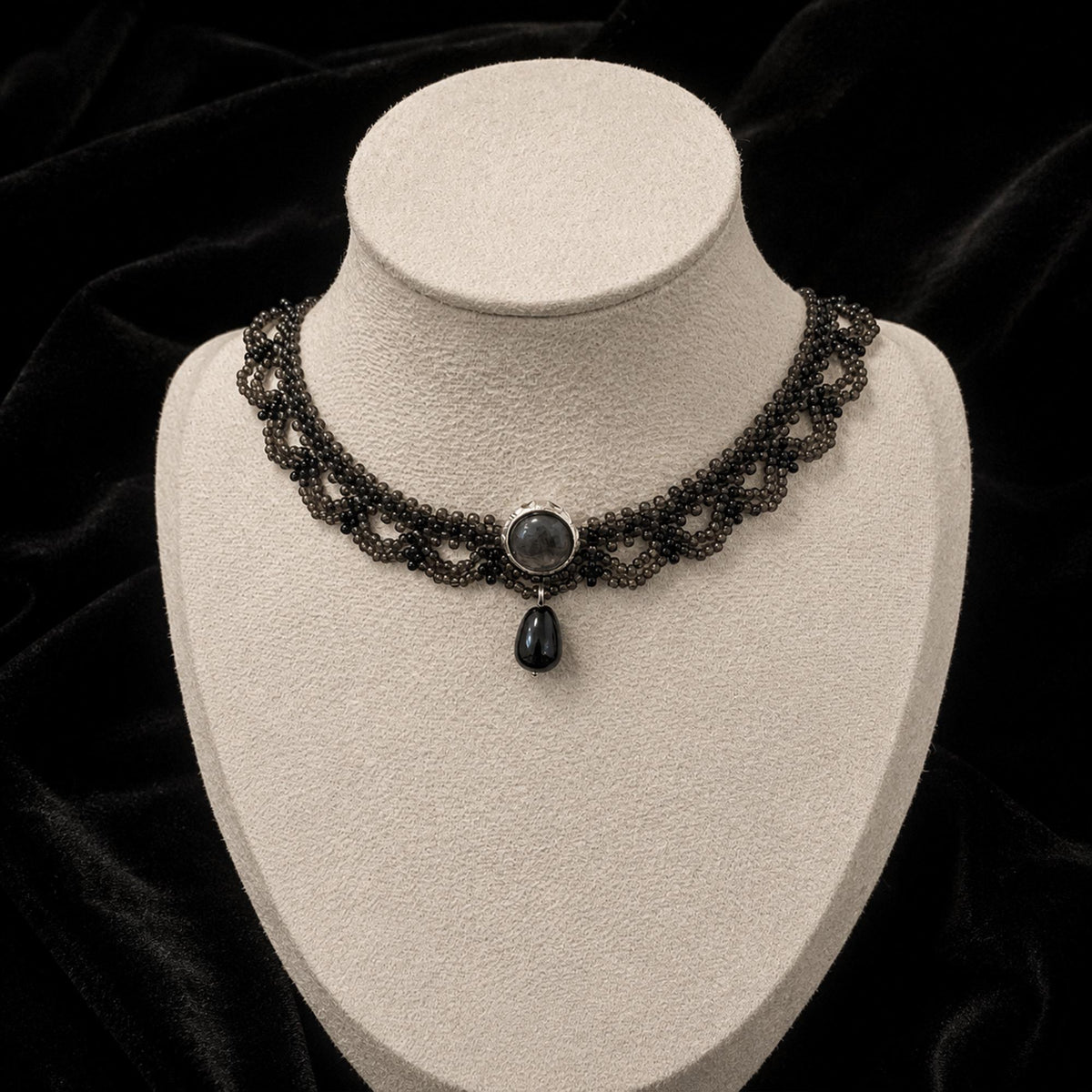 Black beaded lace-pattern necklace with a dark teardrop pendant on a jewelry bust.