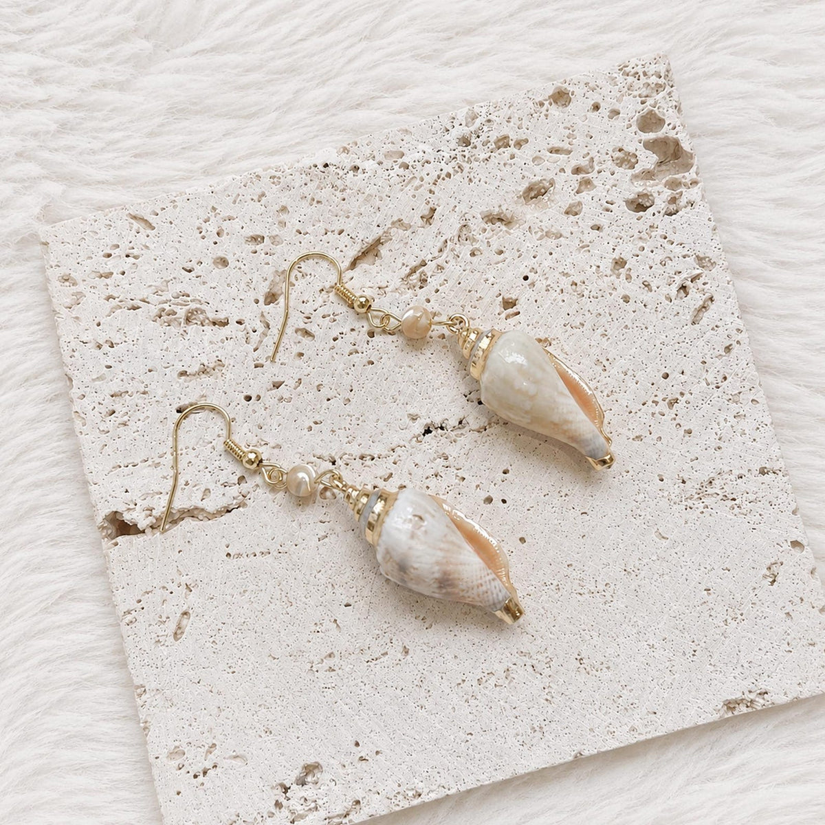 Angled close view of pointed natural shell earrings with pale reflective surfaces.