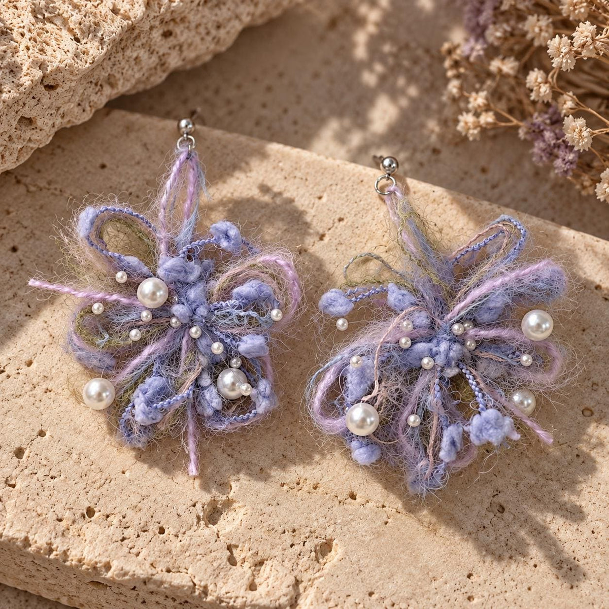Pair of lavender looped-yarn flower earrings with white pearl-like beads on pale stone.