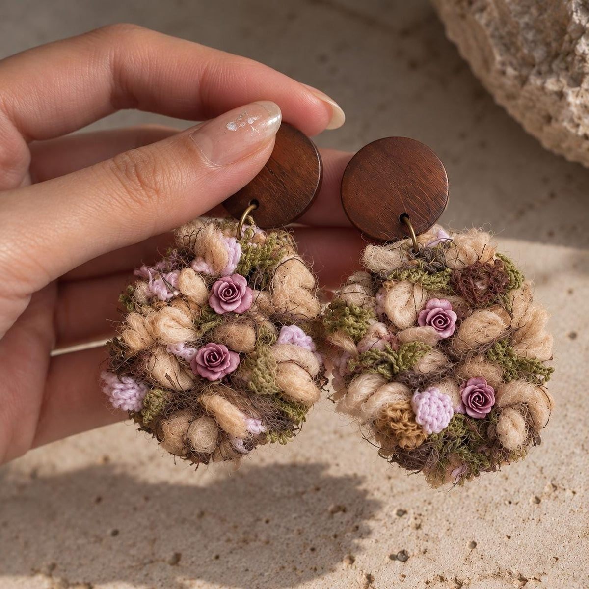 Pair of yarn floral earrings with brown studs held in a hand.