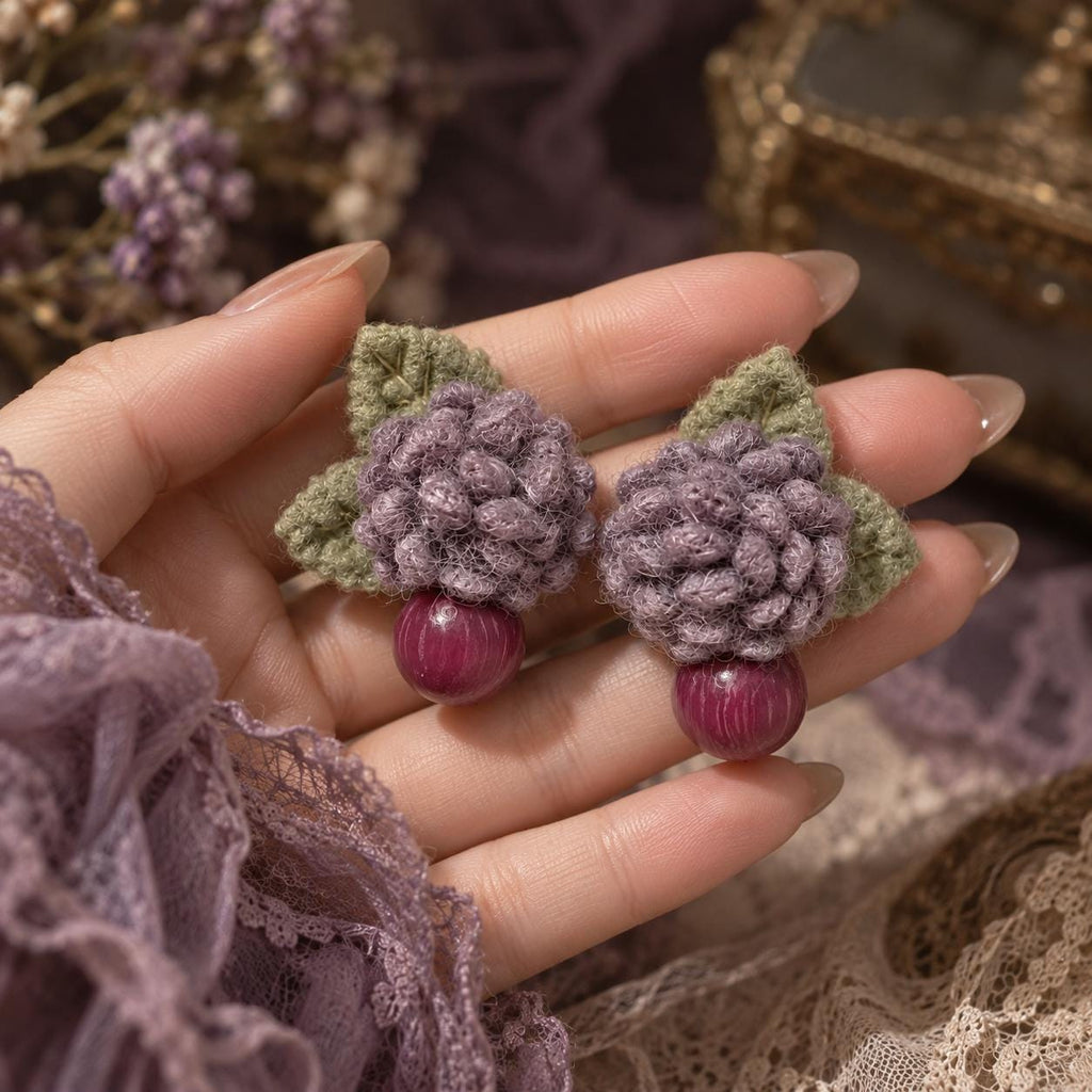 Pair of Lilac Berry lavender crochet-flower earrings with magenta bead drops held in a hand.