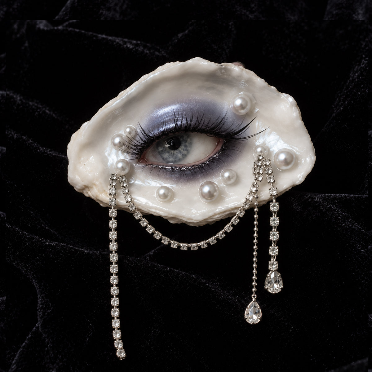 Methyst Haze oyster-eye jewelry with black lashes, pearl-like beads and dangling chains on black fabric.