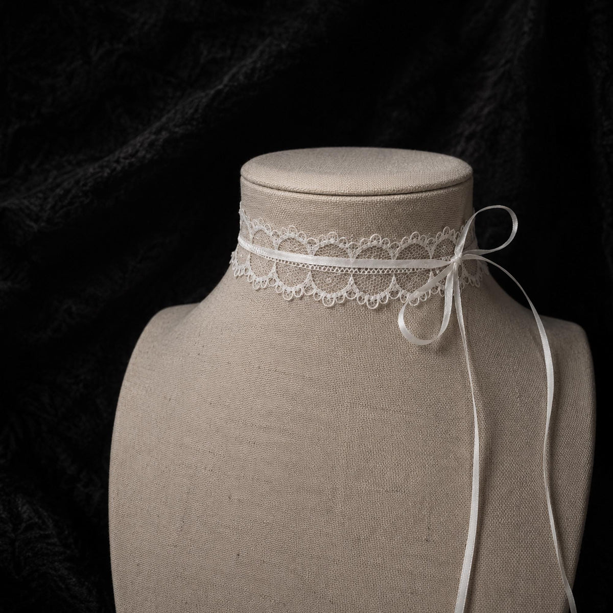 Fine white lace choker tied with a bow on a jewelry bust.