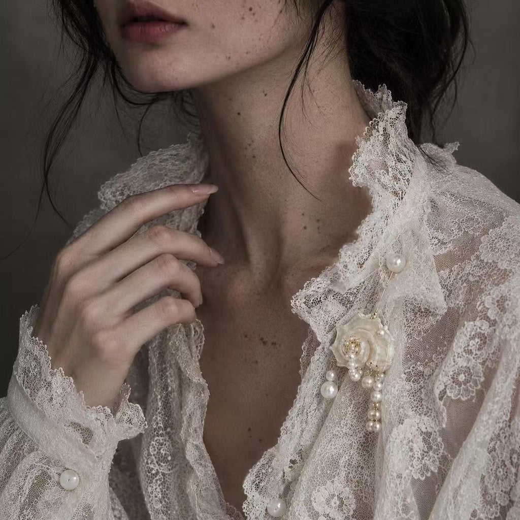 Conch-shell brooch with hanging pale beads pinned to ivory lace.