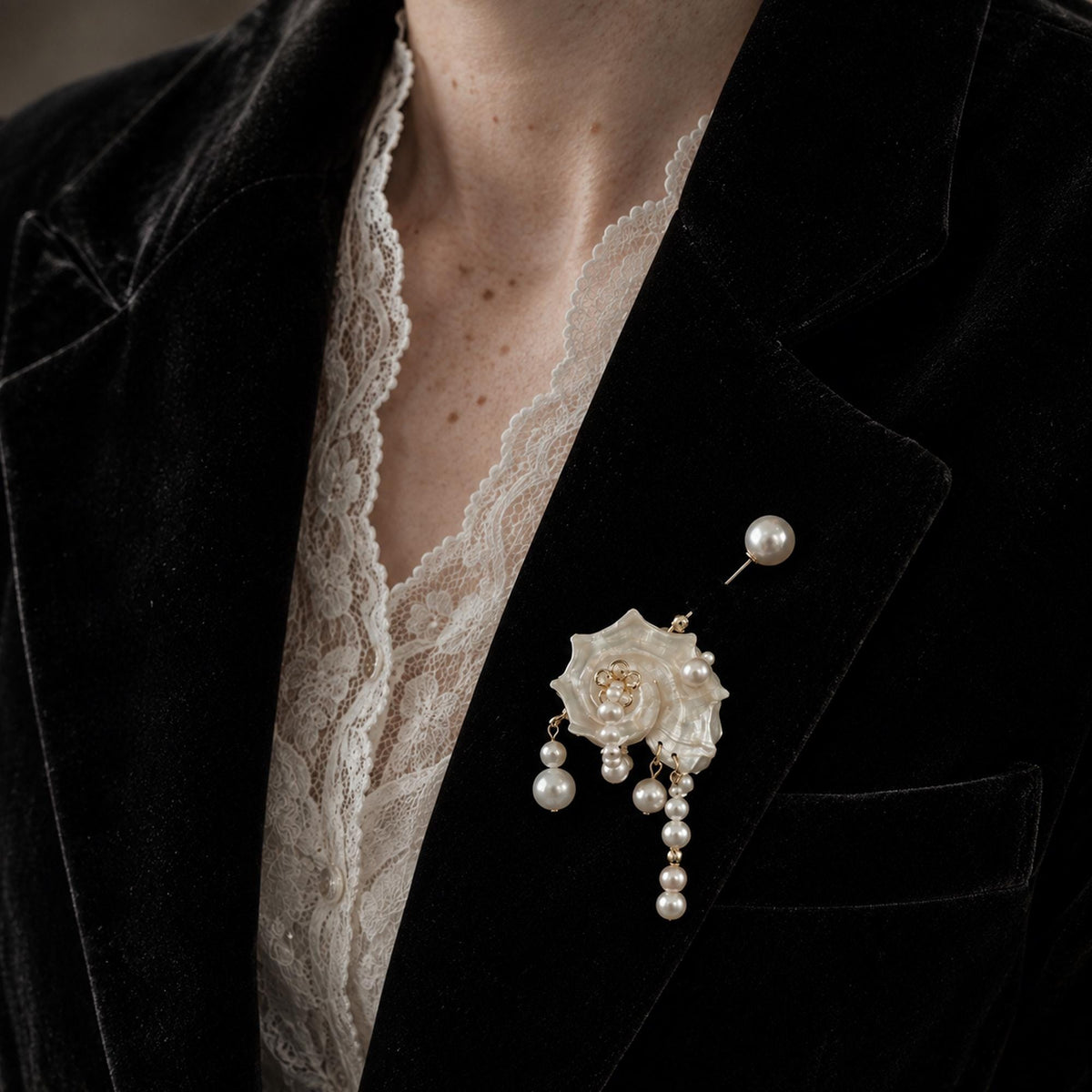 Conch-shell brooch with hanging bead strands and a pearl-topped pin worn on a dark blazer.