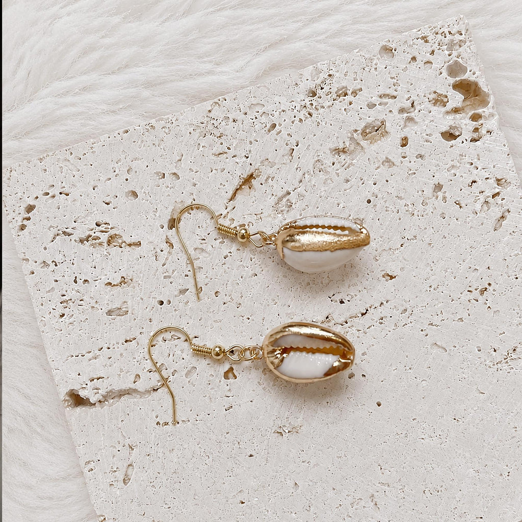 Pair of pale cowrie-shell earrings with gold-tone rims and natural slit openings.