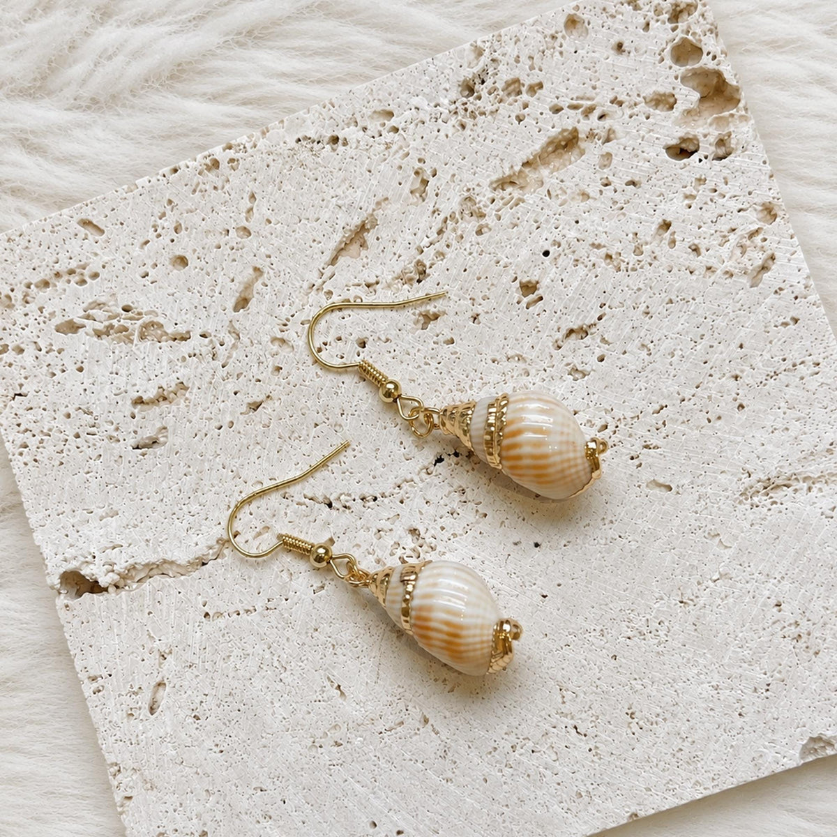 Angled view of ribbed pale shell earrings with warm-toned tips.