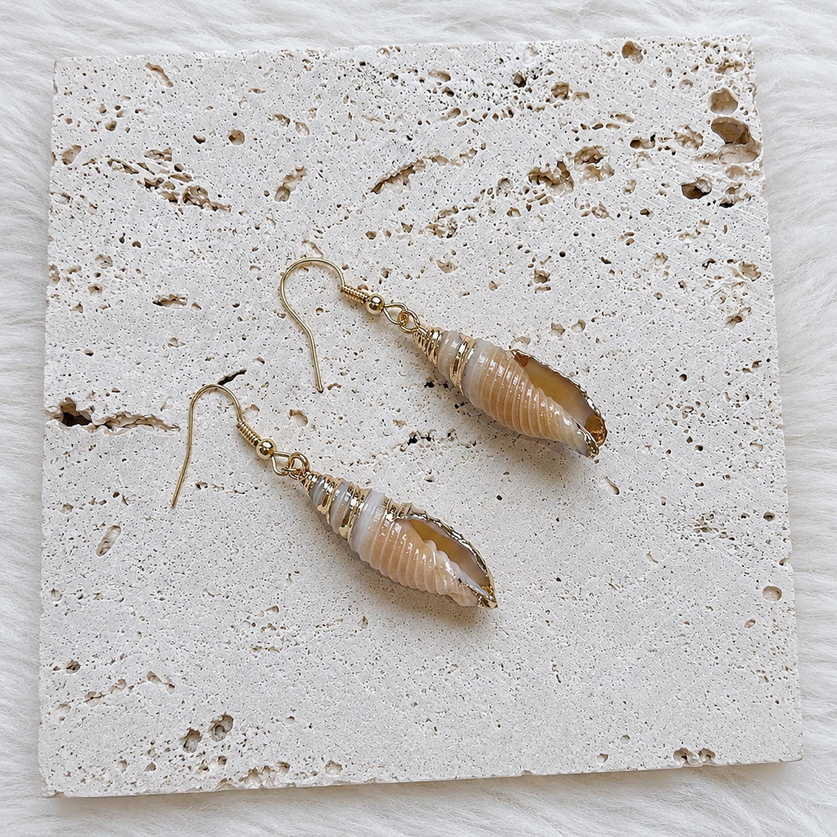 Pair of elongated spiral conch-shell earrings in warm brown tones.