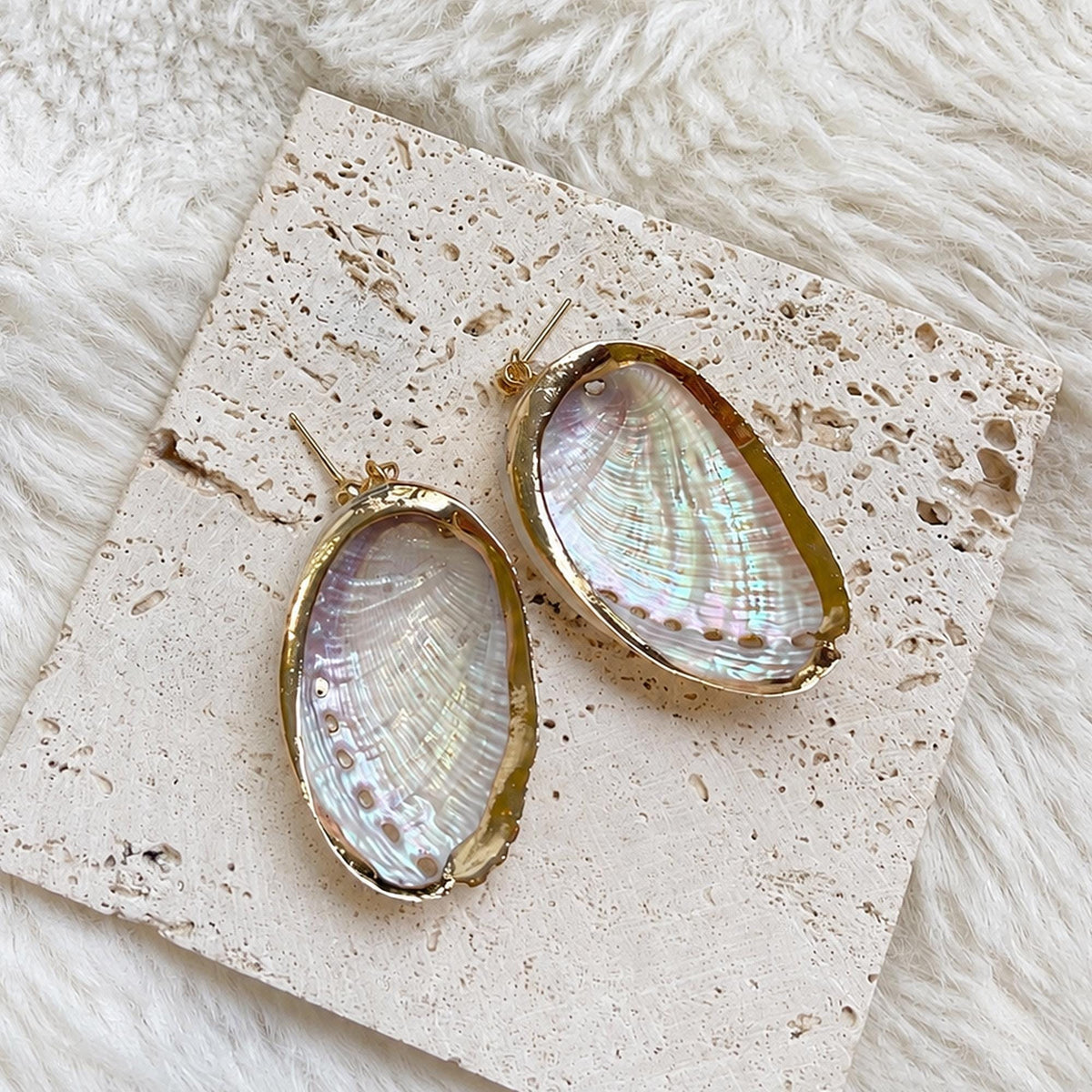 Reverse view of oval shell earrings showing their pale reflective interiors and gold-tone rims.