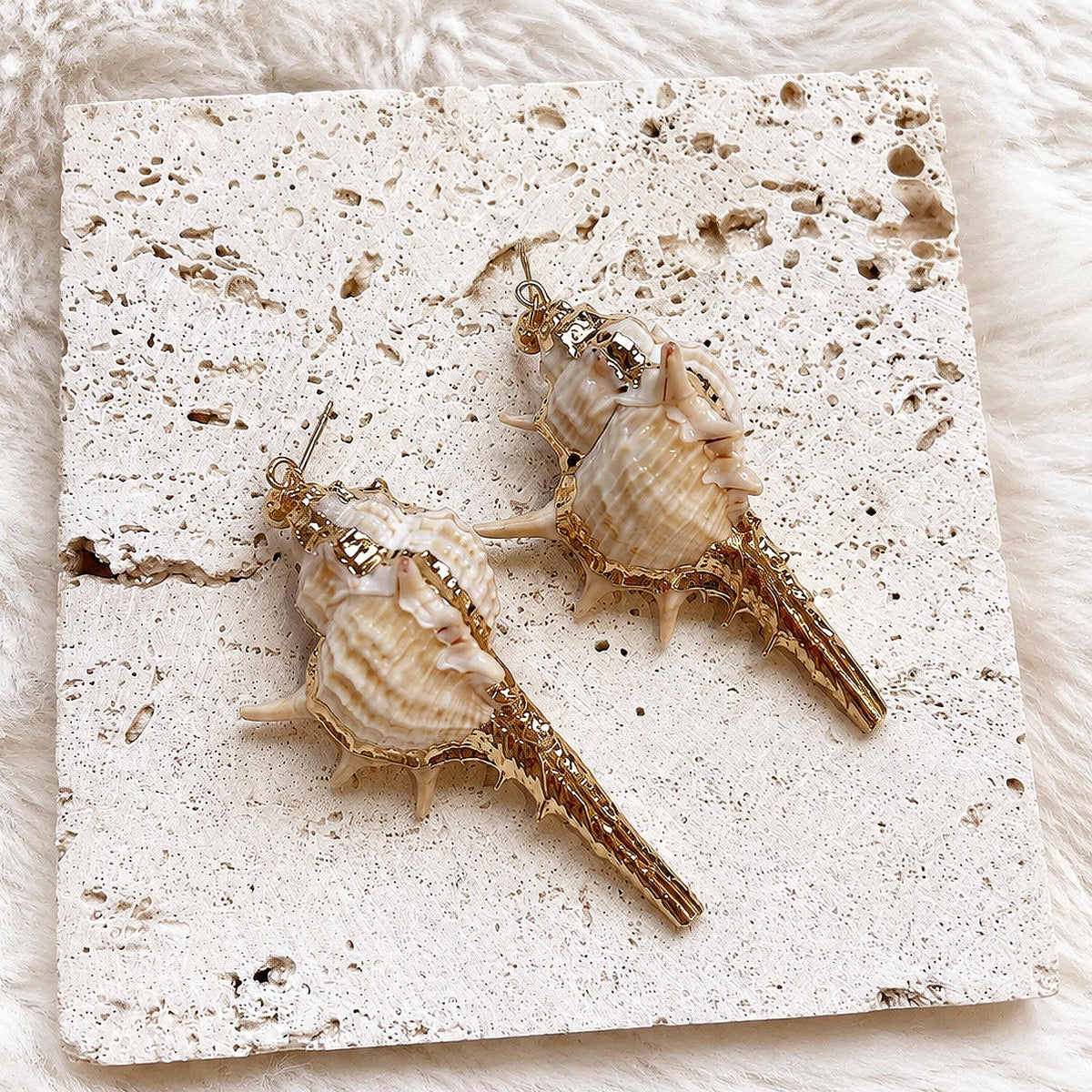 Pair of long spiked conch-shell statement earrings on cream lace.